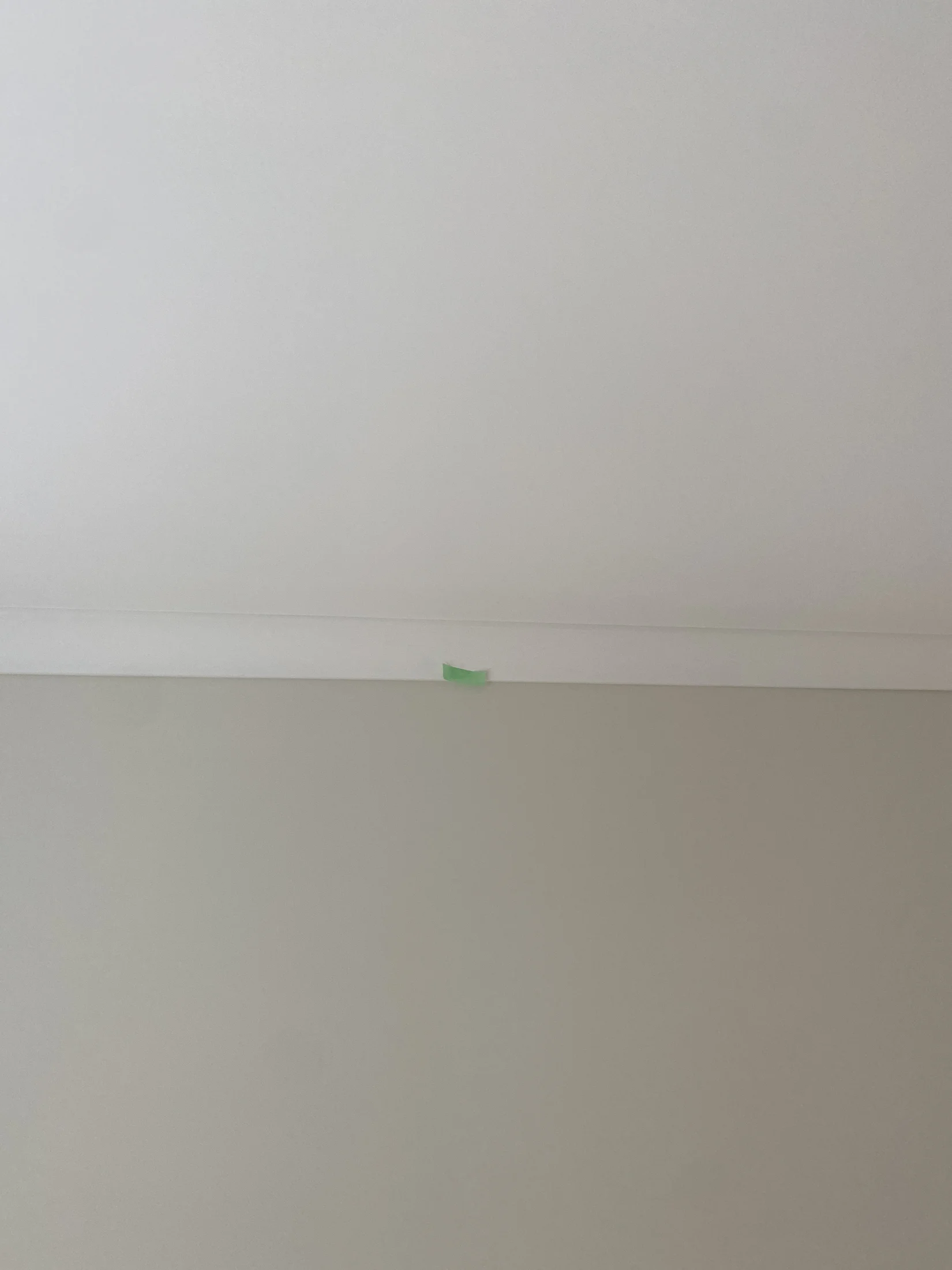 A small piece of green tape is stuck on a white and beige wall near the ceiling. The setting is minimal and neutral.