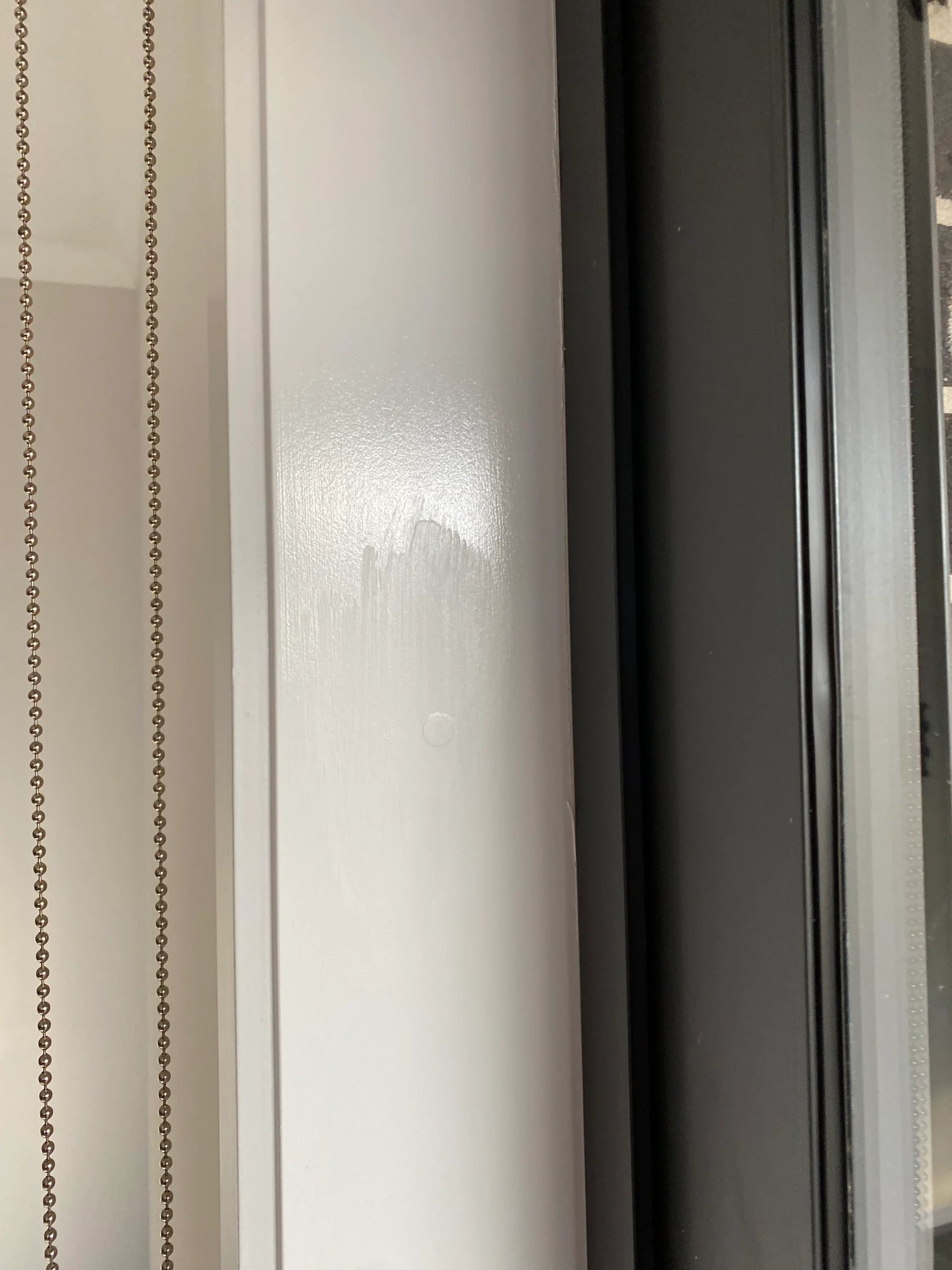 Vertical blind cords hang beside a white-painted window frame. The background is brick, creating a contrast between light and dark tones.