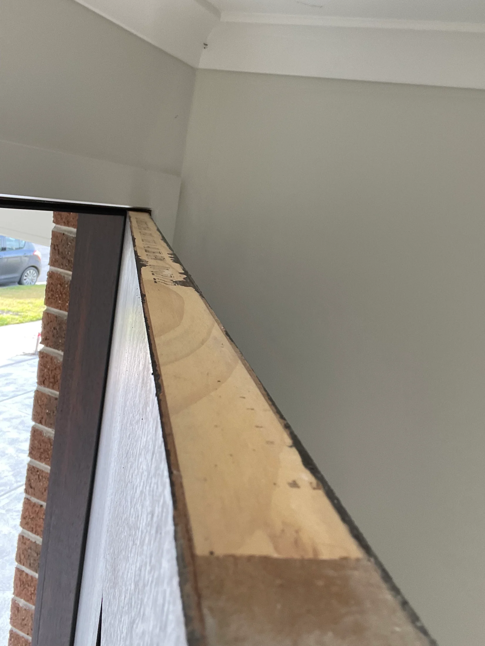View of a sloped roof edge against a gray wall, with a red brick wall to the left. Part of a parked car is visible in the background.