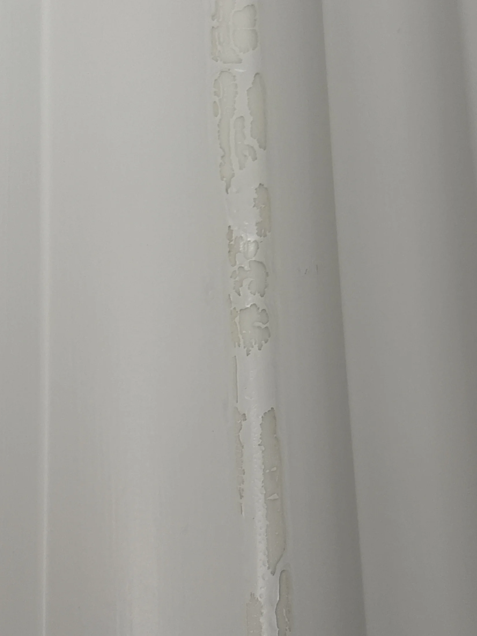 Close-up of a white textured surface with peeling paint along a vertical line, showing underlying material. No visible text or patterns.