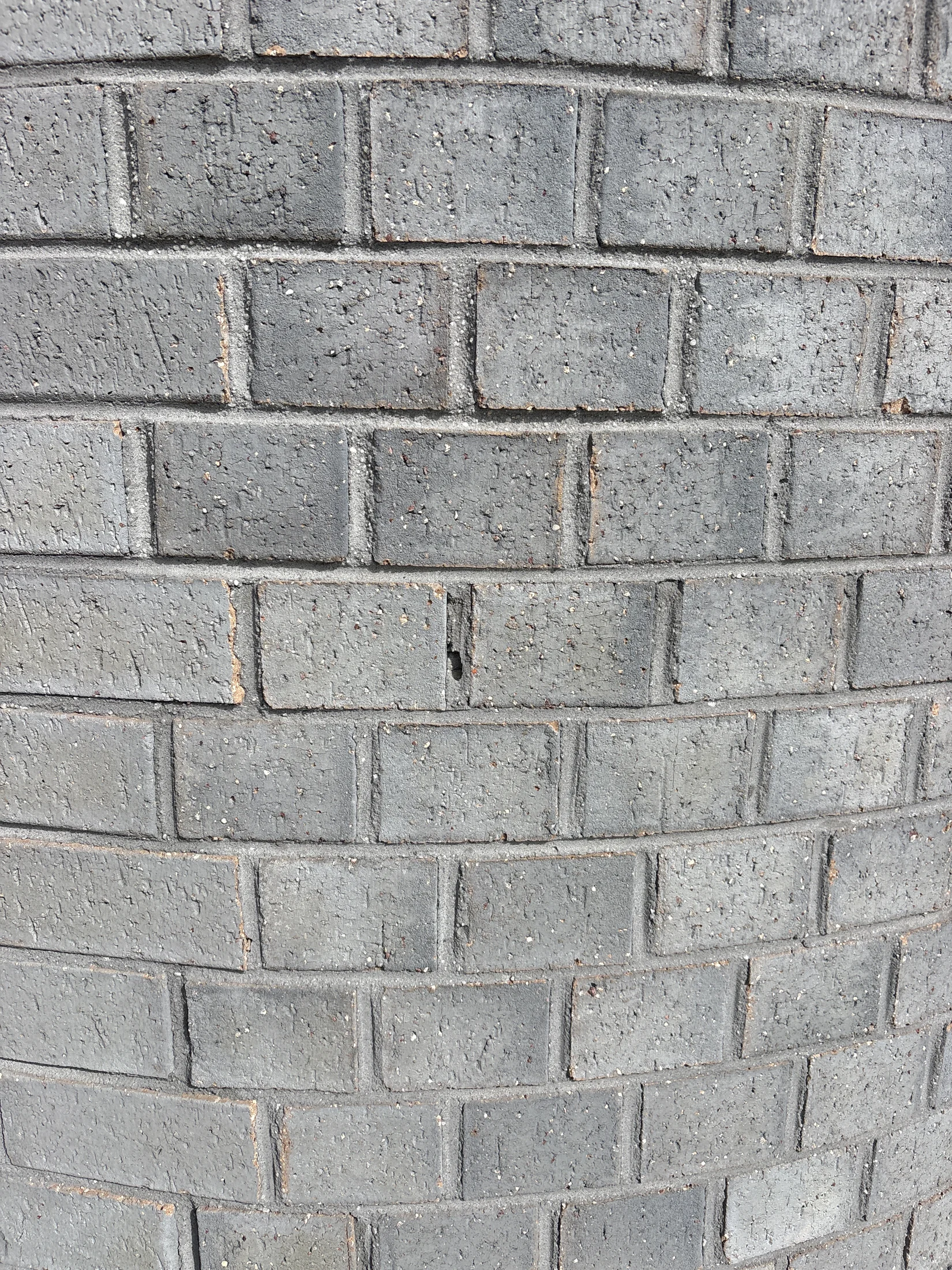 Curved gray brick wall with a rough texture and visible grout lines, showing subtle color variations in natural light.