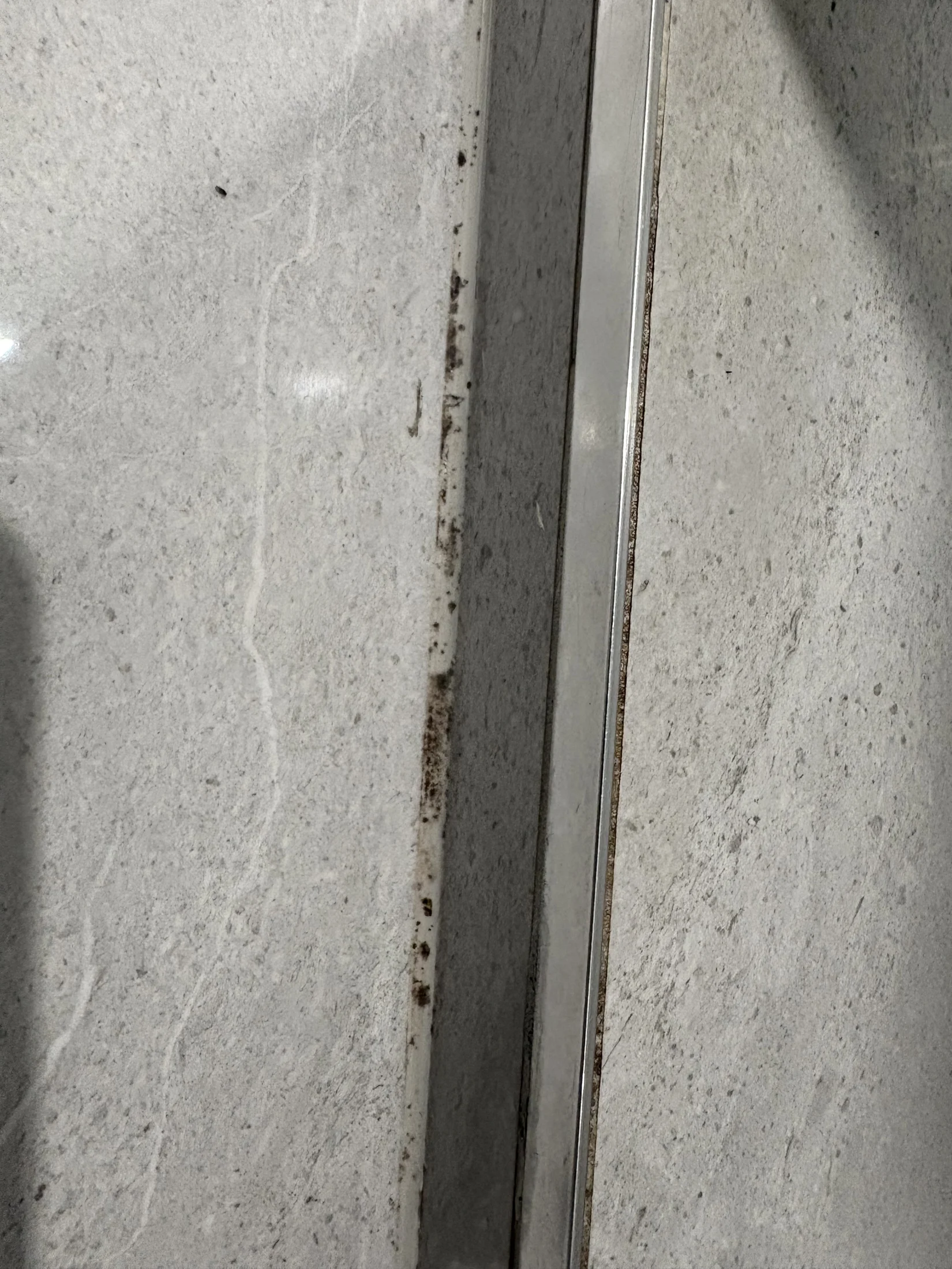 Close-up of a gray, textured wall with rust stains near a shiny metal edge. The setting appears industrial or construction-related.