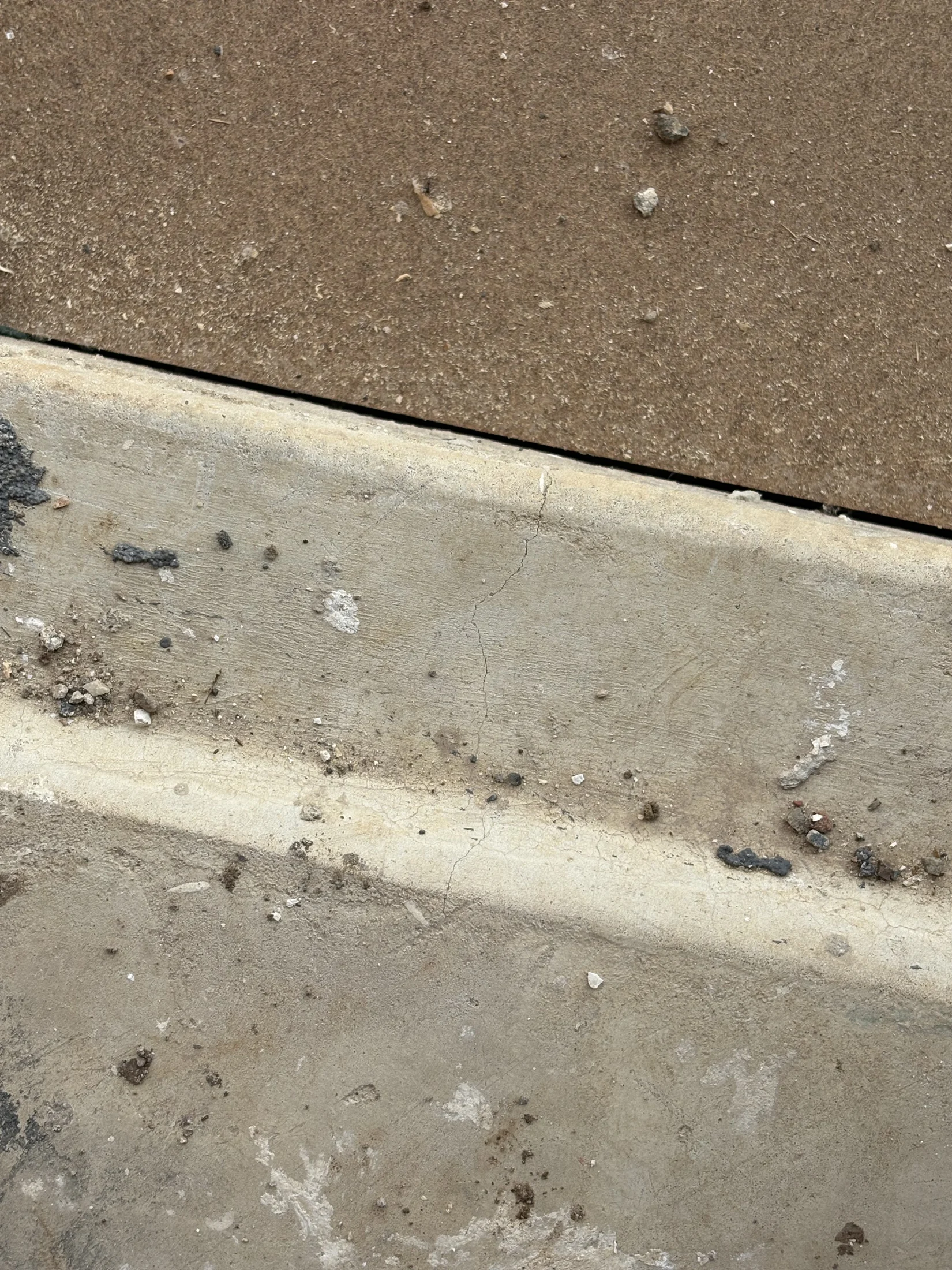 Cracked brown and gray concrete surface with scattered small rocks and dirt. Weathered texture, no visible text or movement, rustic mood.