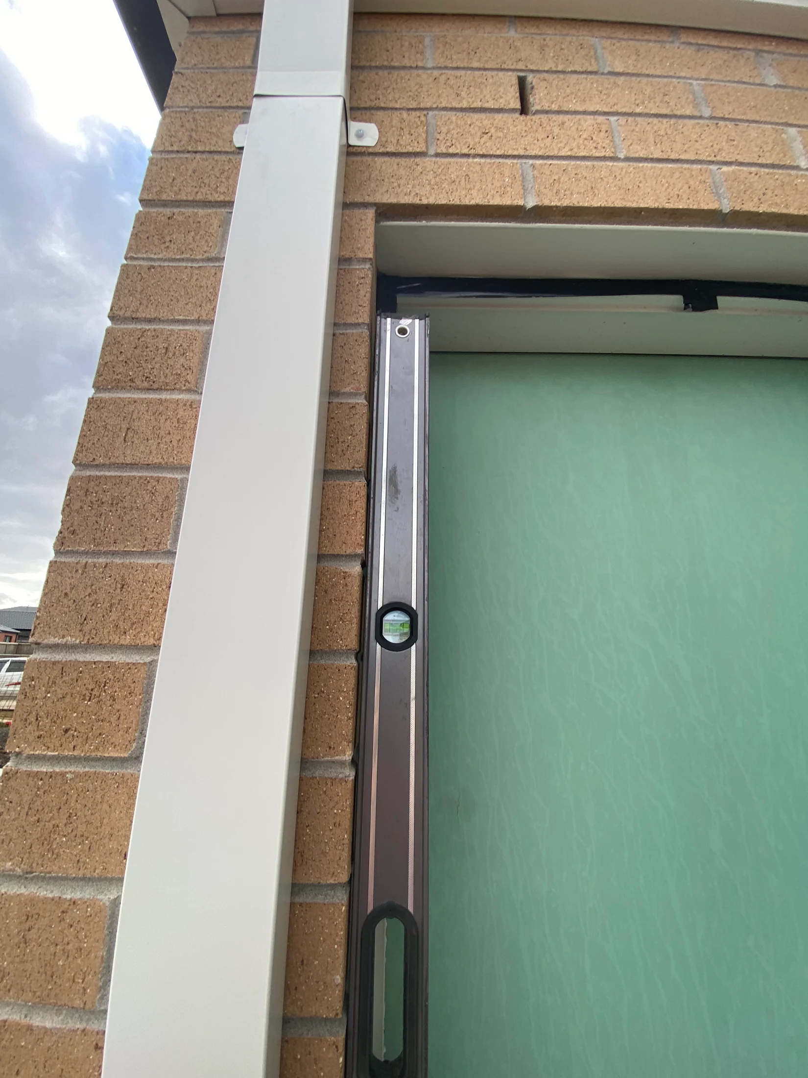Level tool against a brick wall with a green door on the right. The cloudy sky is visible, creating a calm atmosphere.