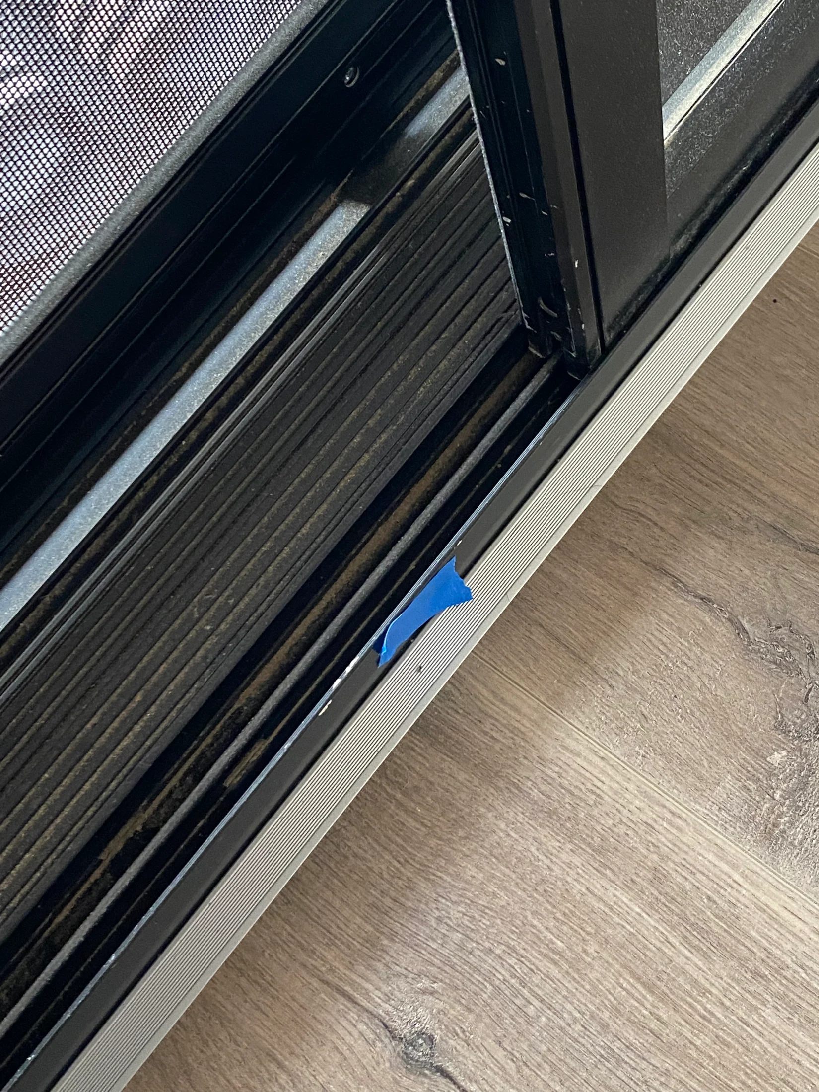 Laminate flooring edge with silver aluminium trim up against powder coated black framed sliding door