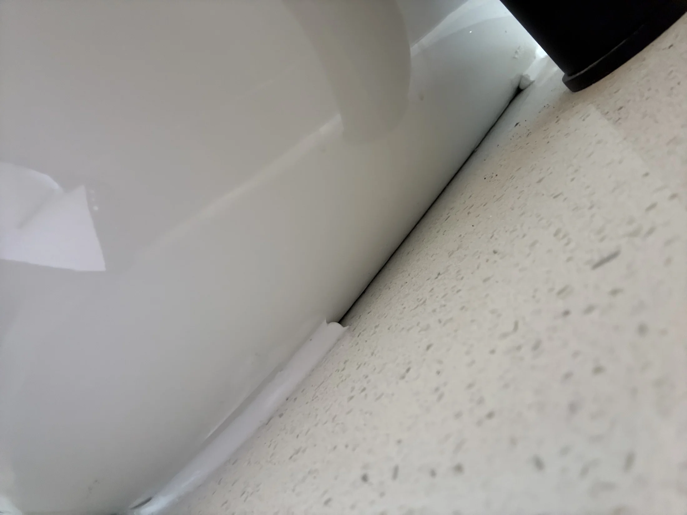 White bathtub edge with a black object near white, speckled tile floor. The close-up image shows a clean, minimalistic setting.