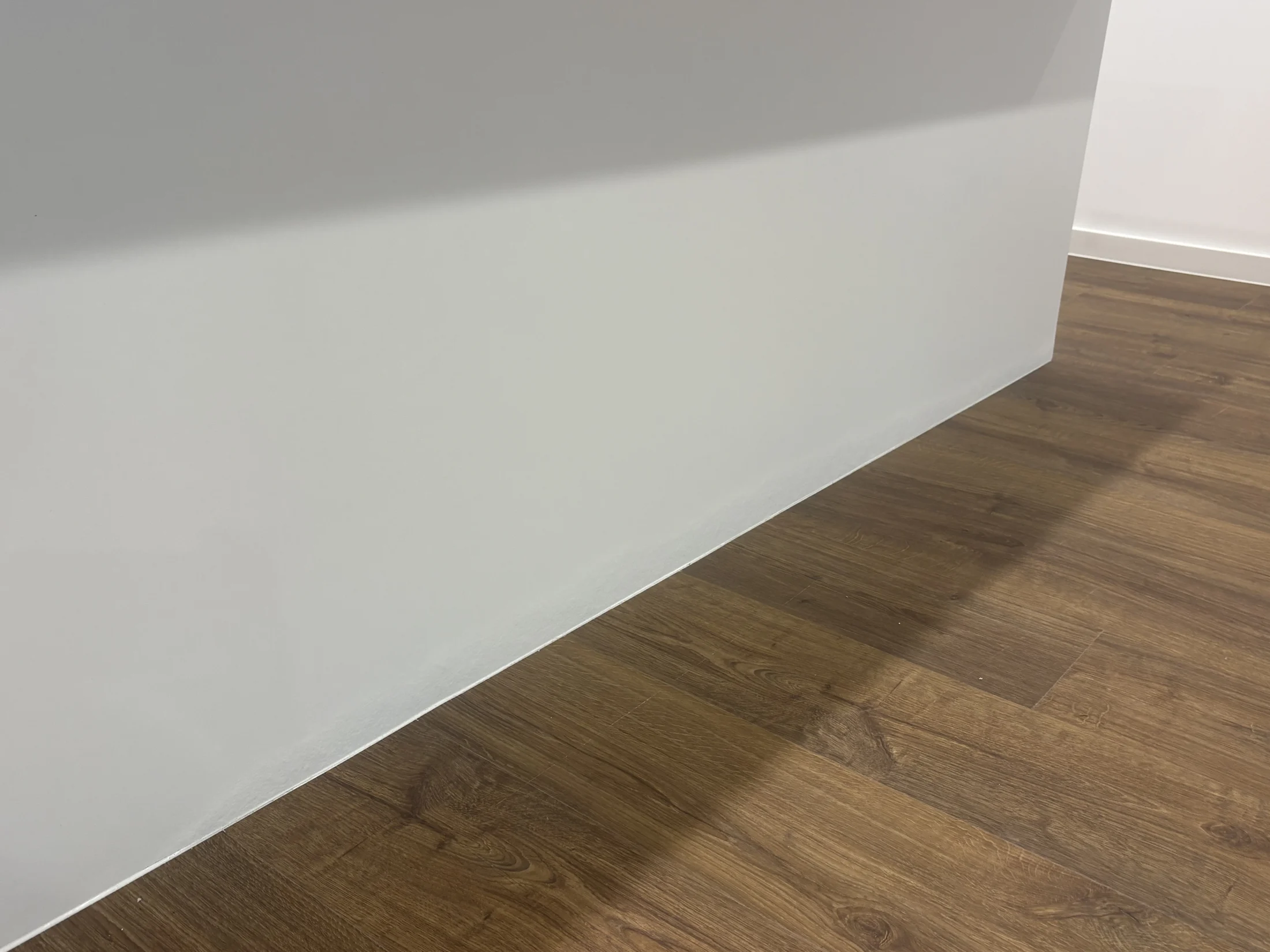 A white wall meets a brown wooden floor. The setting is minimalistic with soft lighting, creating a calm atmosphere. No text visible.