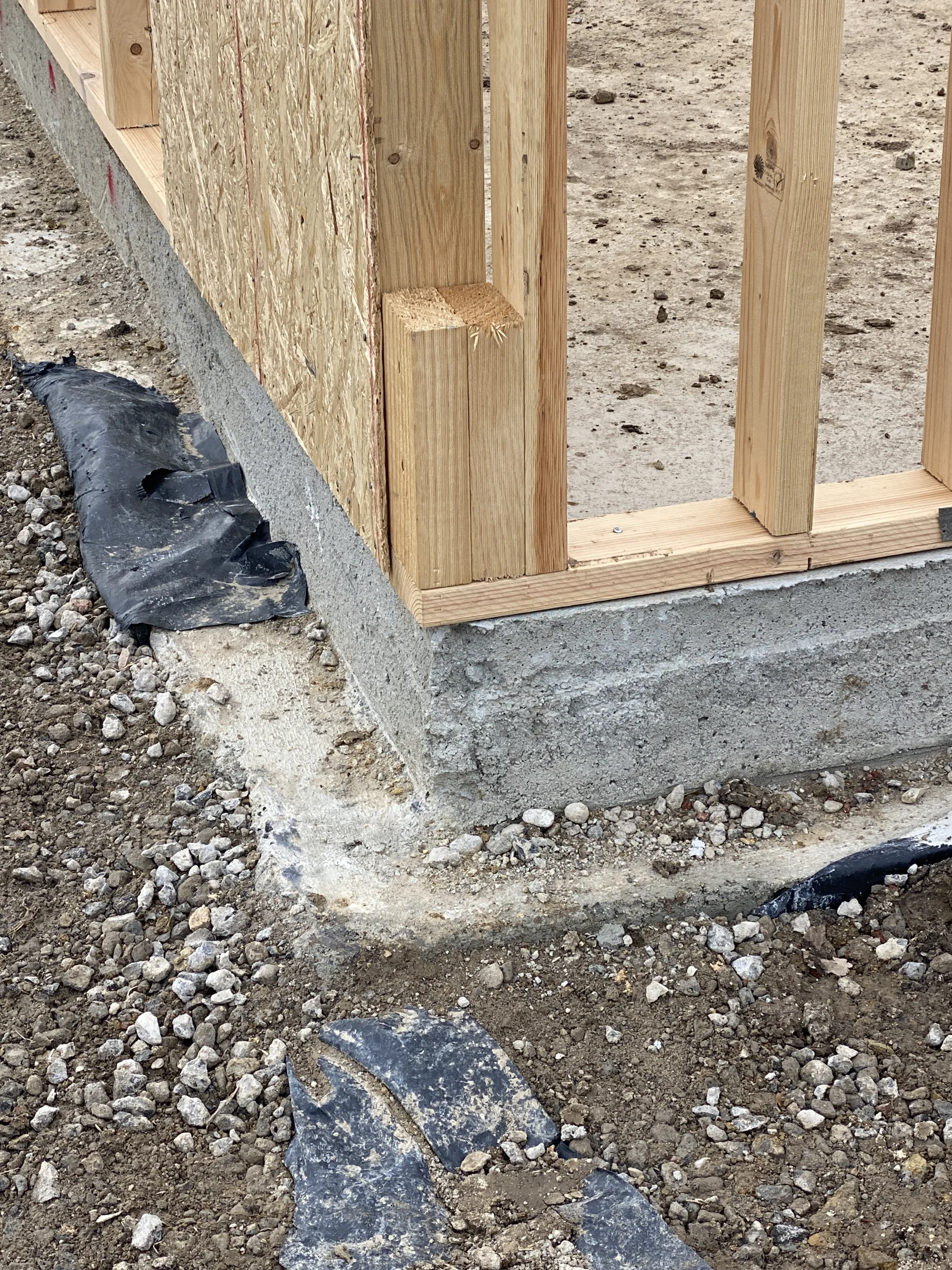 Wooden frame on a concrete foundation with gravel and plastic lining. No visible text. Construction site setting.