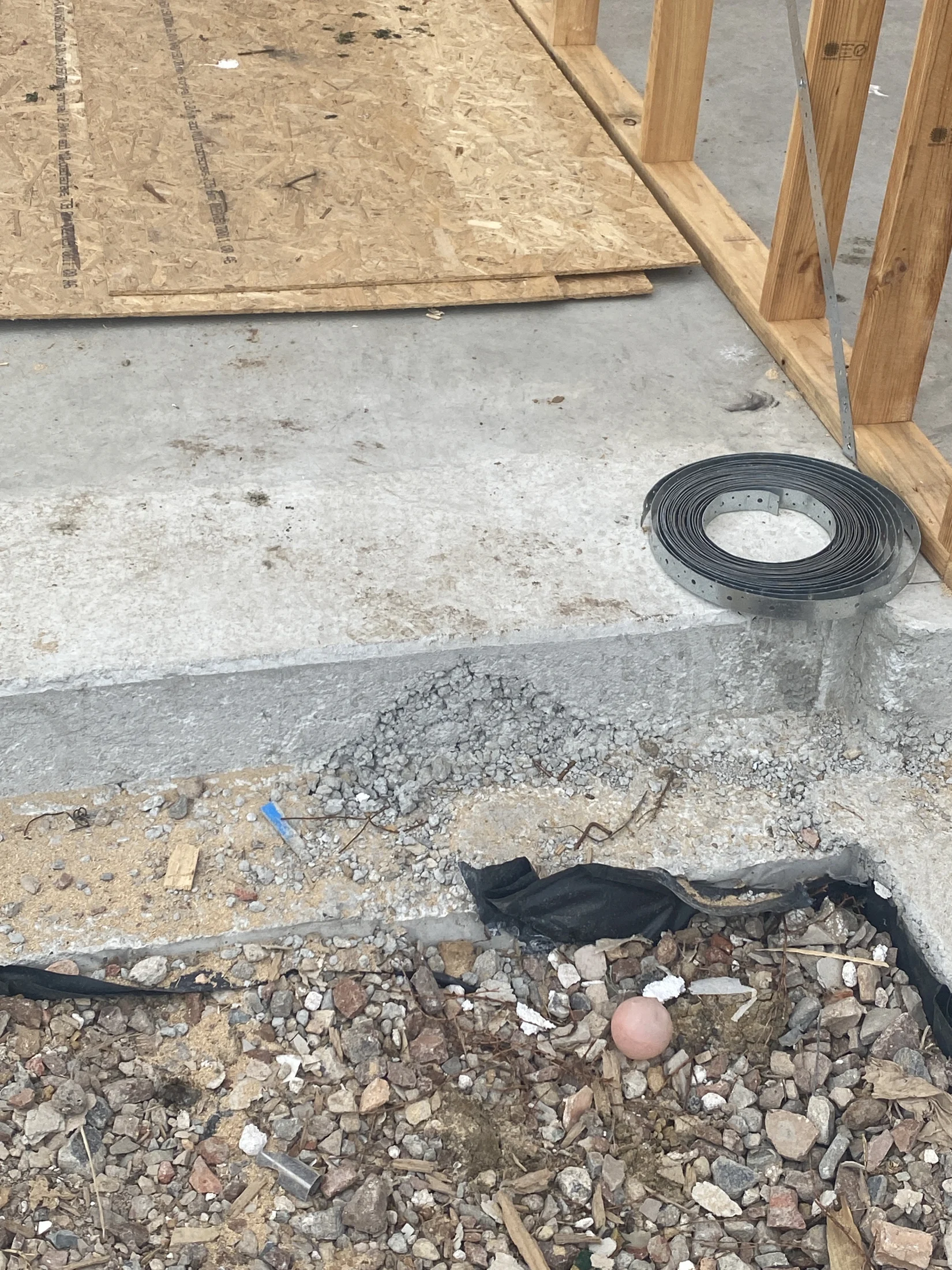 Construction site debris with rocks, wood, and a pink rubber ball. A metal coil and wooden frames are visible. Concrete surface and black cloth.