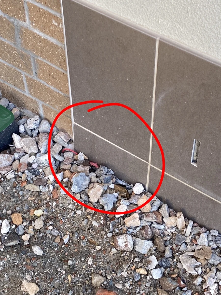 Rocks and gravel at the base of a brick and tile wall. A red circle highlights a specific area. There's a green object partially visible on the left.