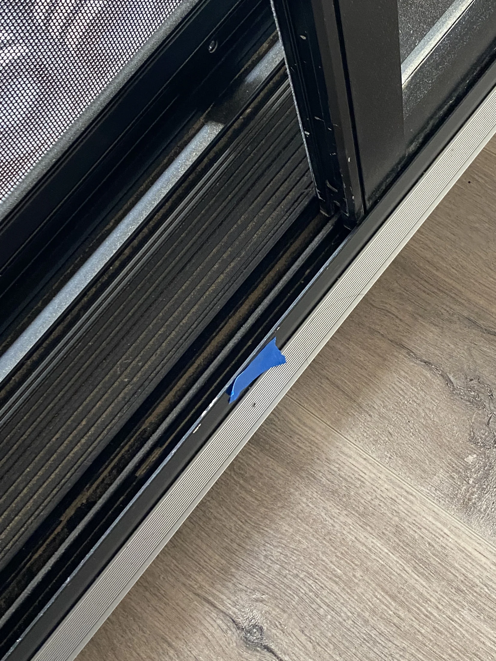 Sliding door track with a small piece of blue tape on the side, set on a wooden floor with visible grain.