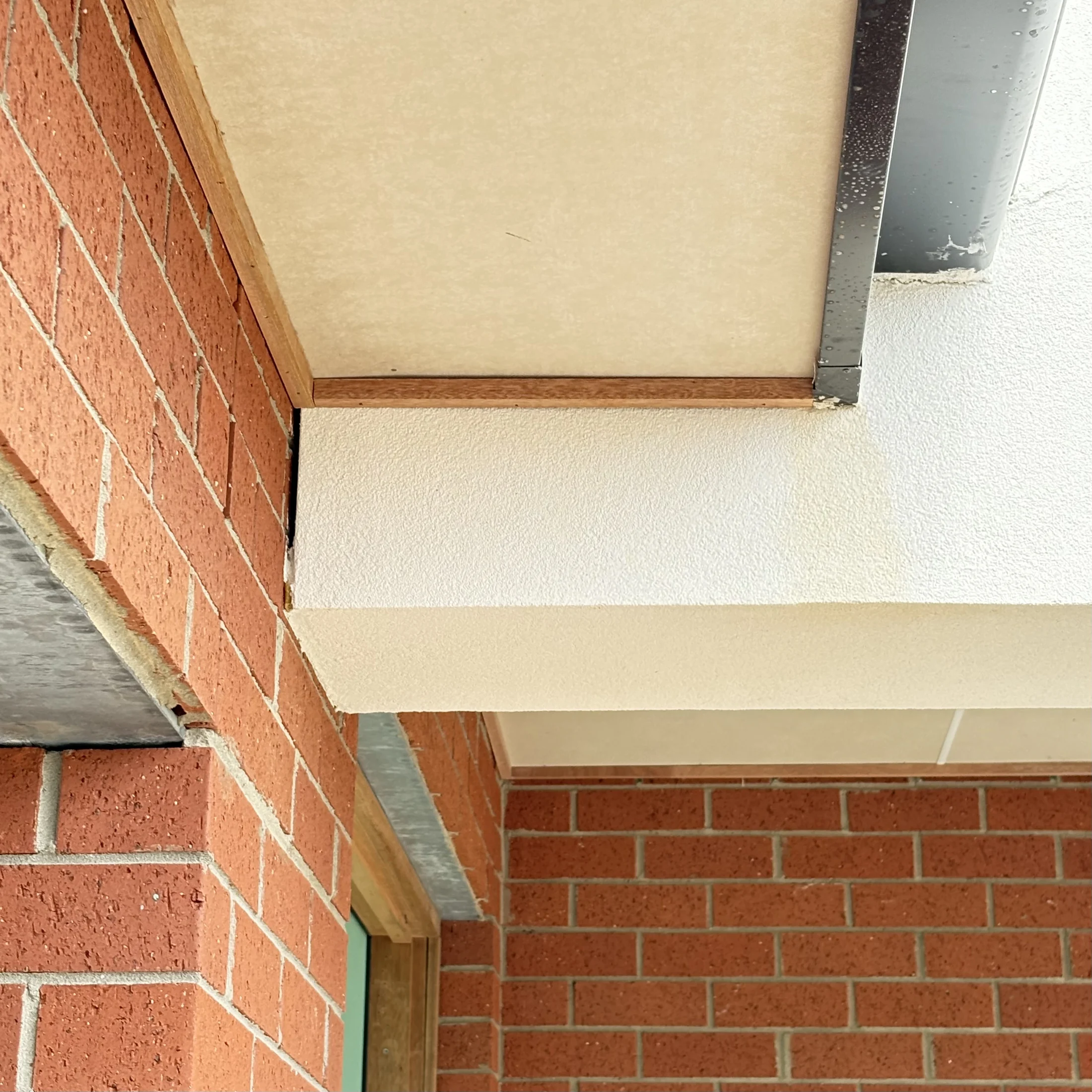 Close-up of a building corner with red brick walls and white overhang. Metal trim highlights modern design. No text or visible subjects.