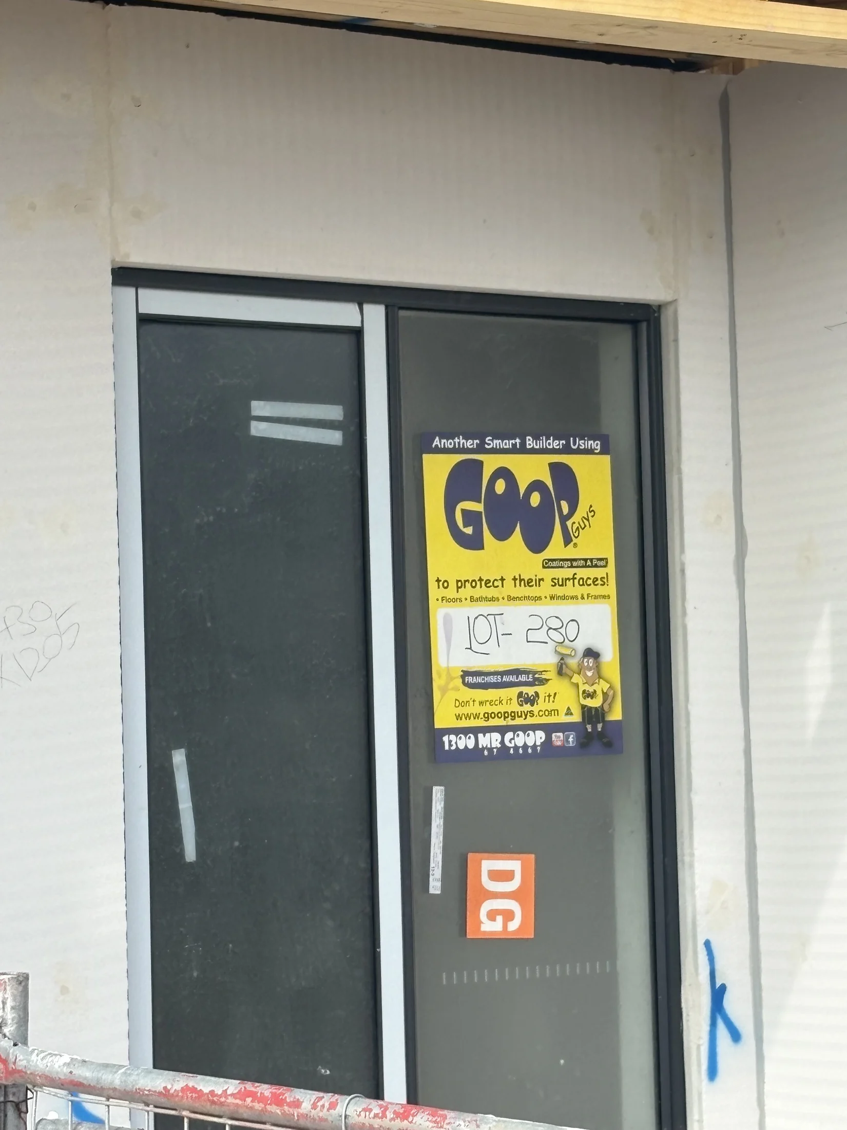 A door with a yellow Goop Guys ad for surface protection features text and cartoon graphics. Nearby is an orange DG sticker.