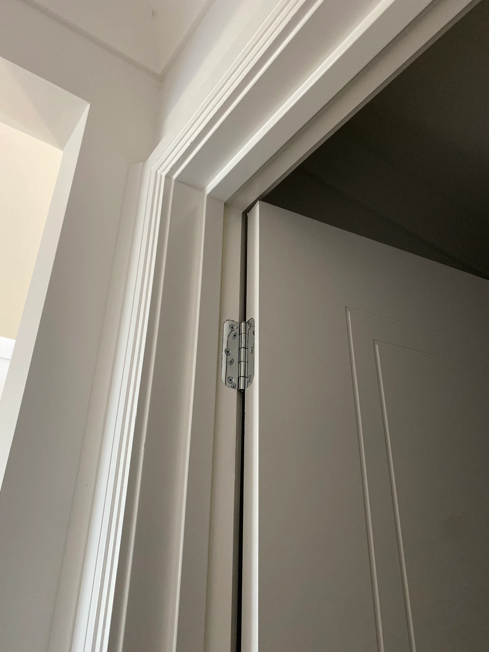 White door half open with silver hinge against a white wall. Minimalistic interior with plain design, creating a calm atmosphere.