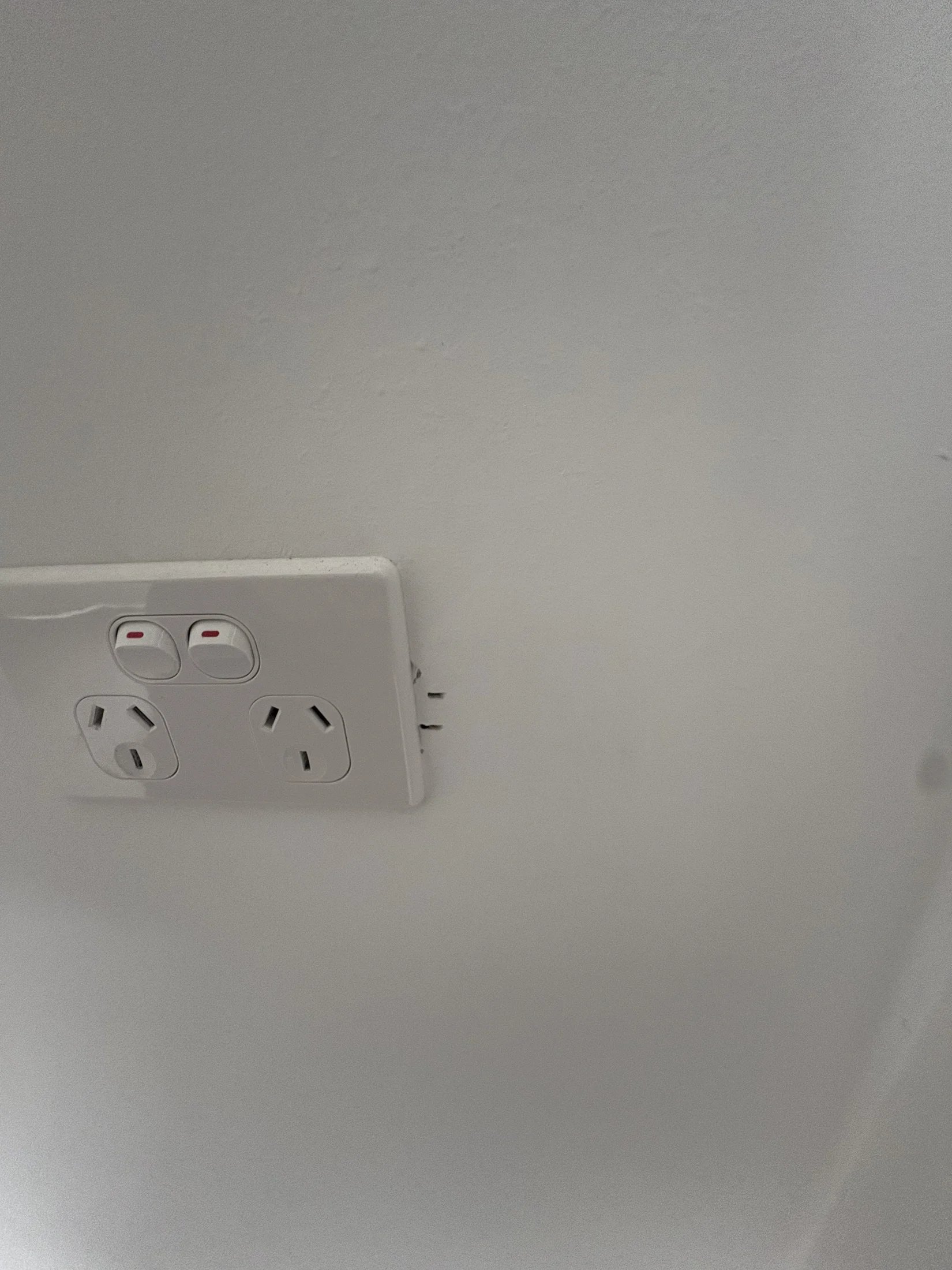 A loose white electrical socket is partially detached from a light gray wall, with visible wires and no text, creating a sense of disrepair.