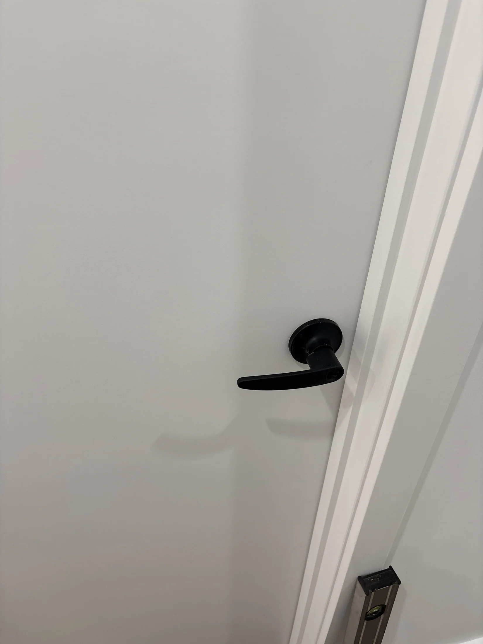 White door with a black handle and a silver level tool on the floor. Calm, minimalistic setting with soft shadows. No text visible.
