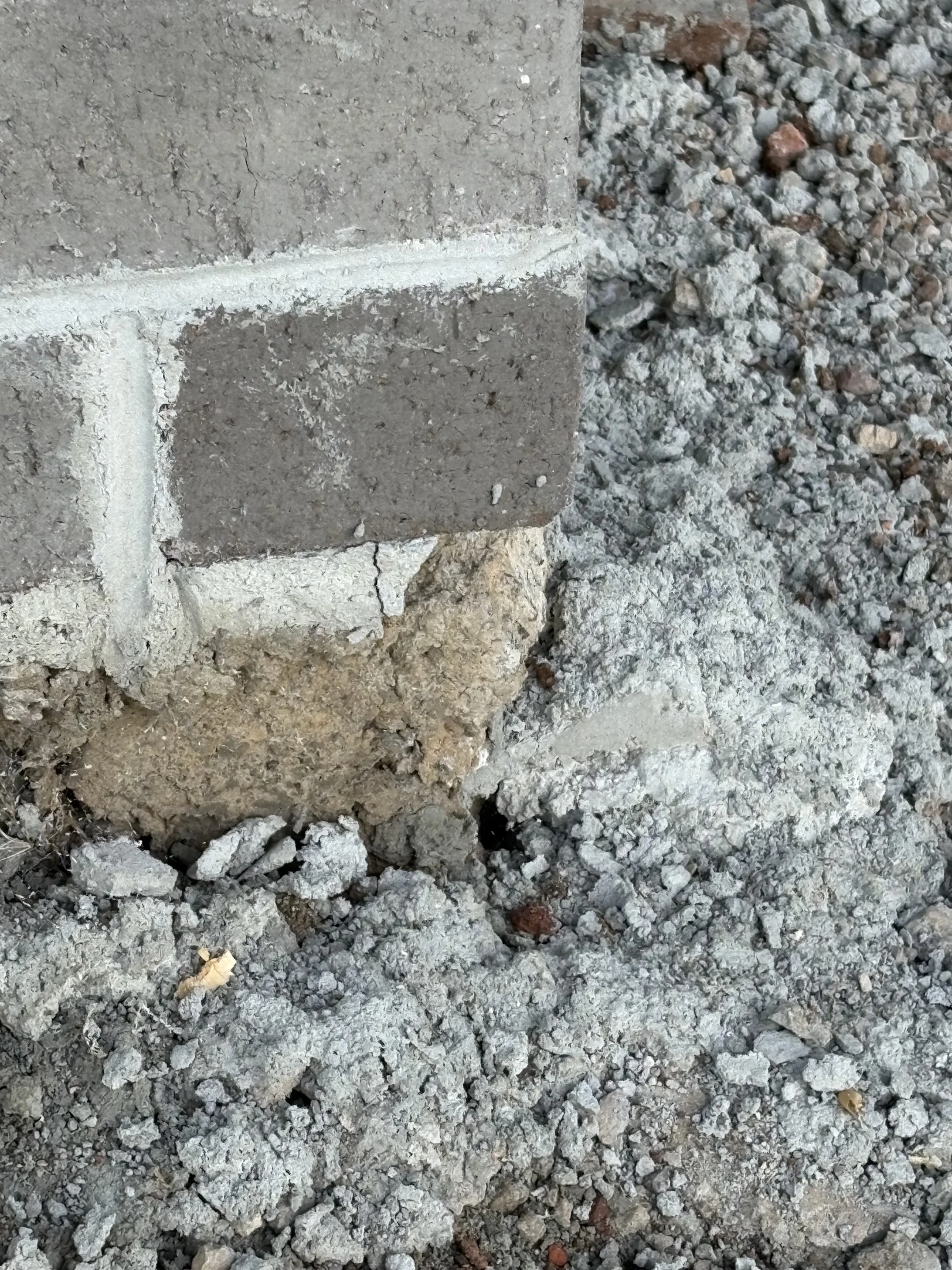 Cracked brick foundation with visible erosion, surrounded by loose gray rubble. The setting appears outdoors, and the mood is concerning.