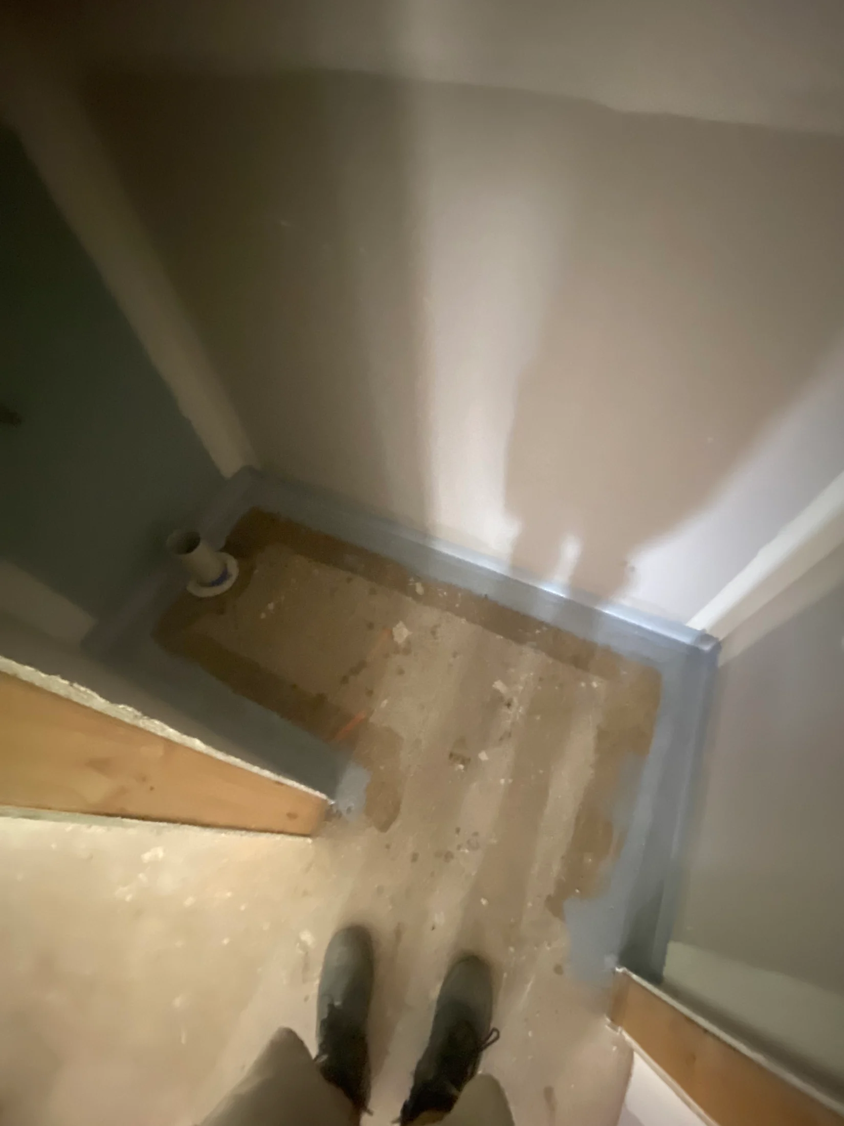 Construction site hallway with dusty concrete floor. Person in work boots visible from above. Dim lighting, shadow on wall. No text present.
