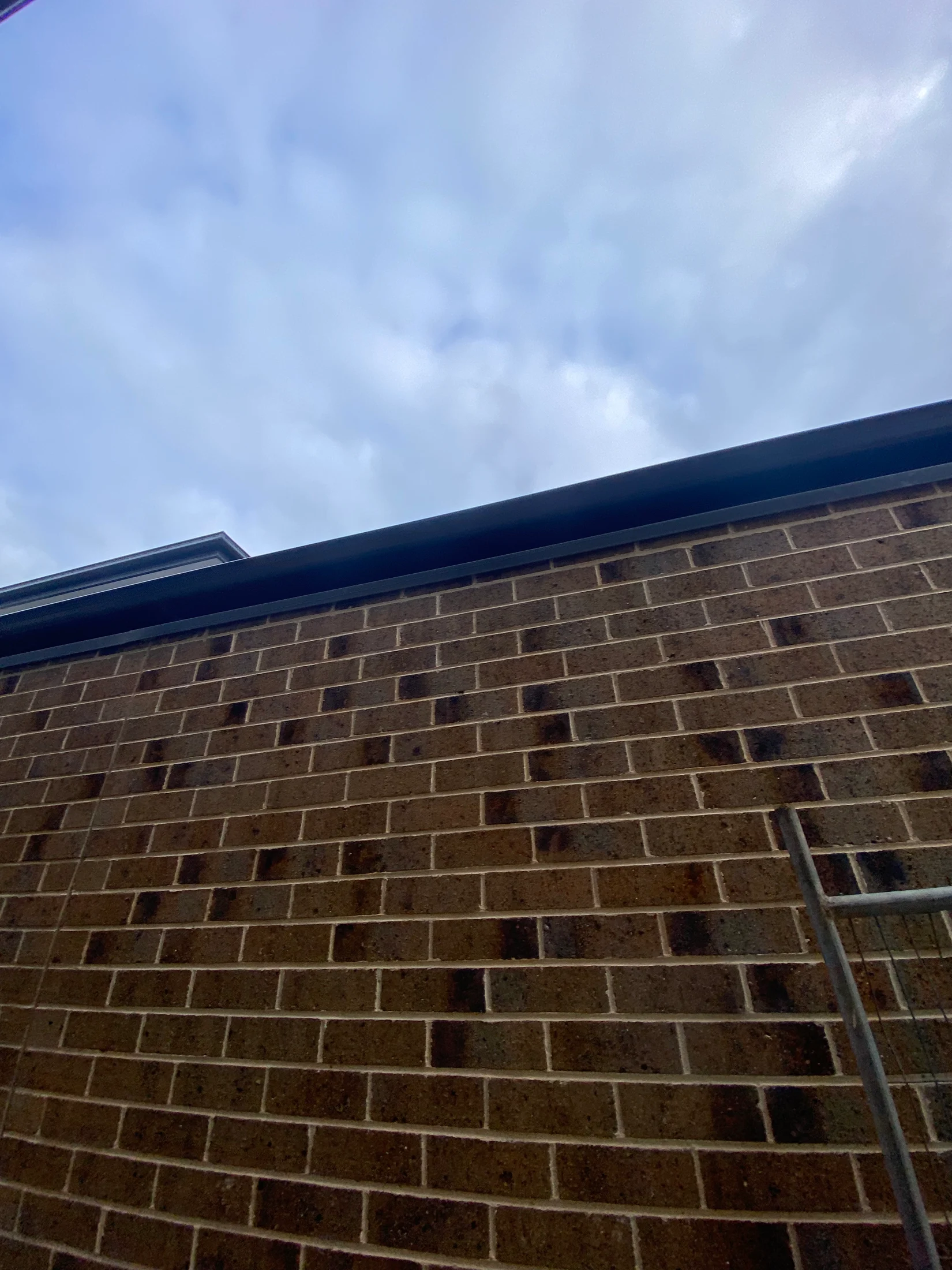 Brick wall under a cloudy sky. No people or actions. Metal rod visible to the right. Overcast atmosphere with a calm, muted tone.