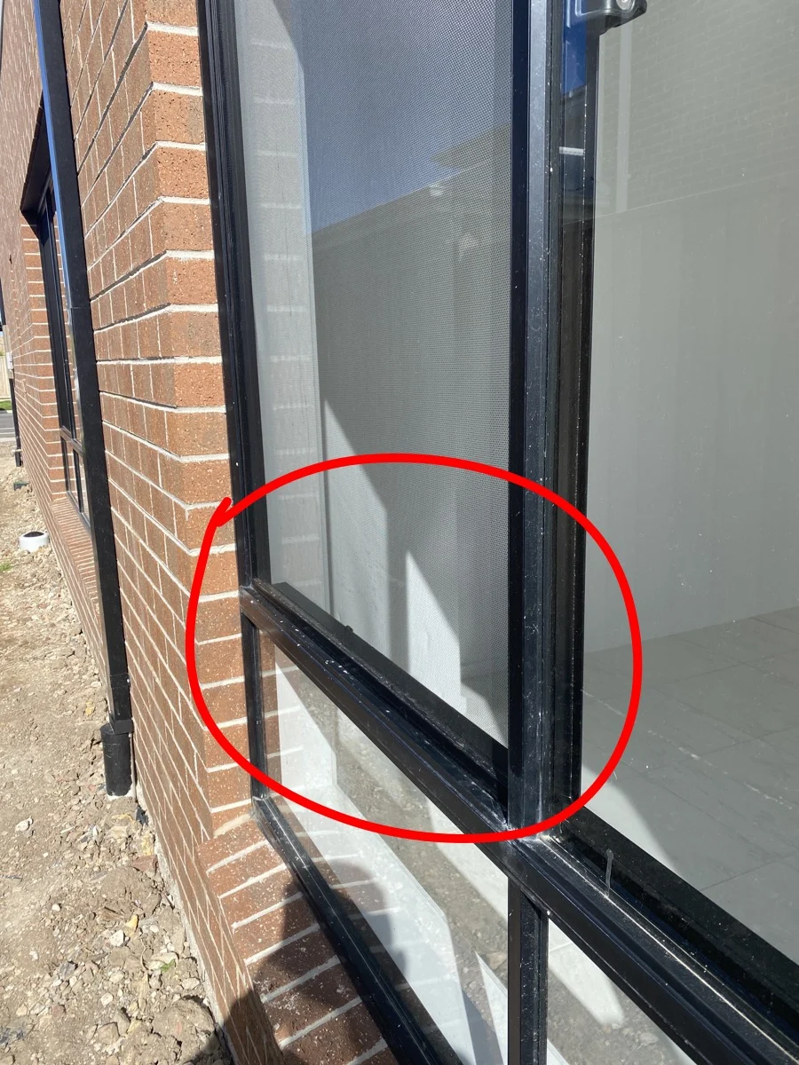 Brick wall with black-framed window, red circle highlighting a screen. Sunlit exterior with dry ground, creating a bright atmosphere.