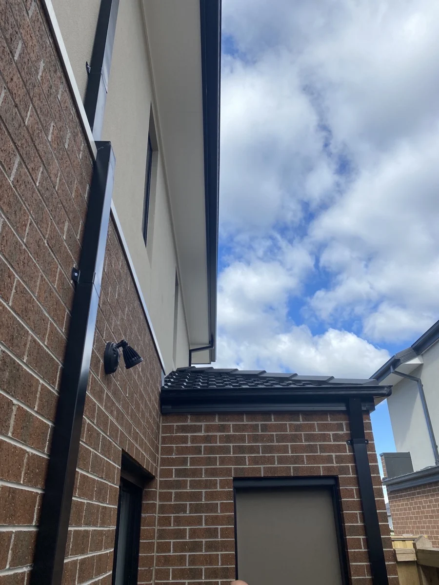 Brick building corner with a security camera, against a cloudy blue sky. Roof tiles visible, creating a calm urban setting.