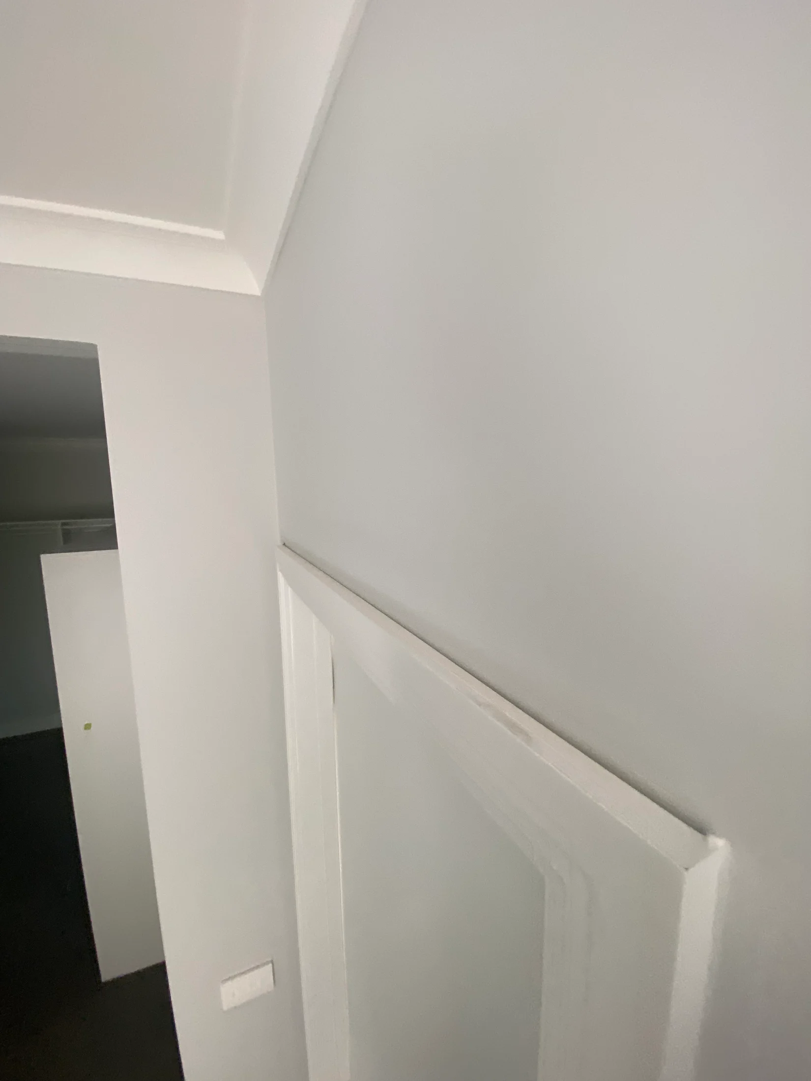 White corner of a room with a doorway, light switch, and closet visible. Walls and ceiling are painted light gray, creating a minimalistic look.