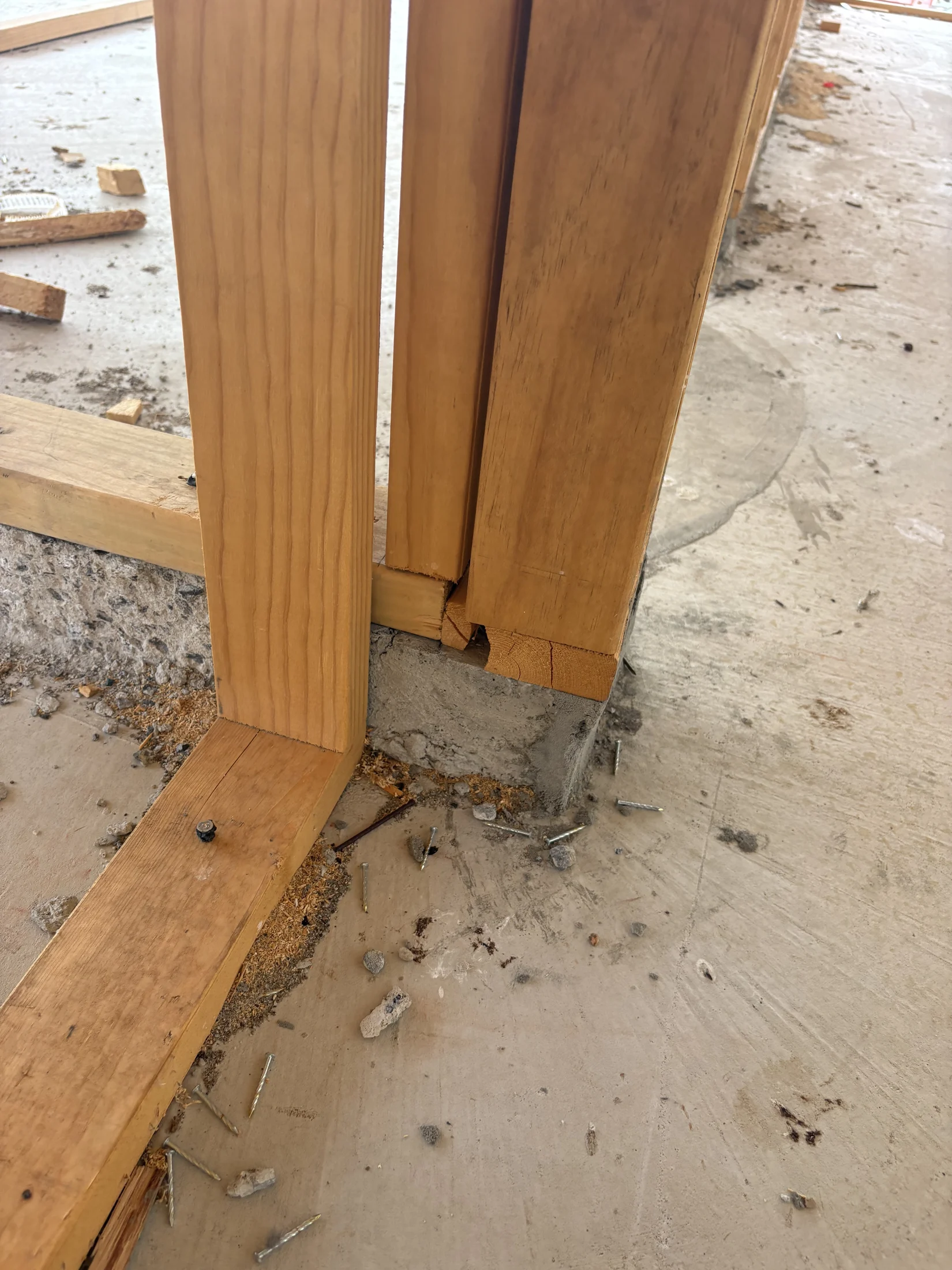 Wooden beams meet a cracked concrete floor with loose screws and debris scattered around, suggesting ongoing construction or repair.