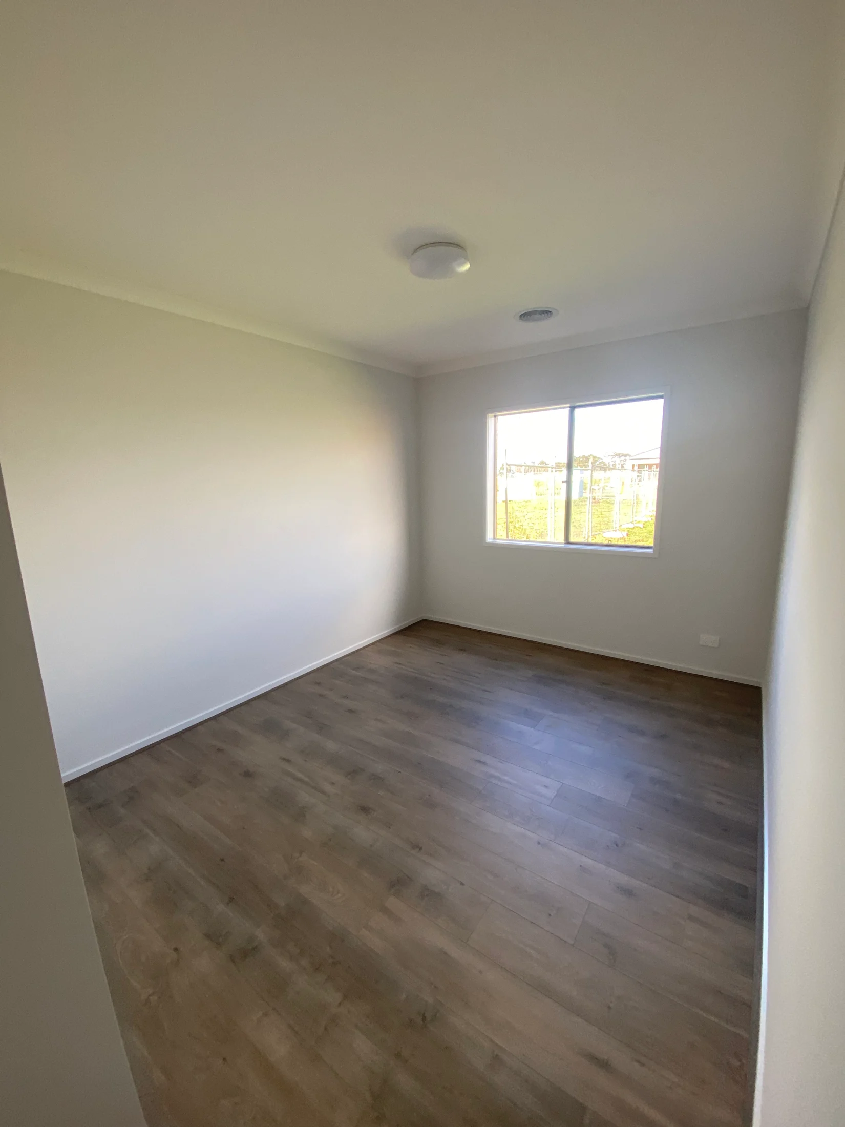 Empty room with light wooden floor, white walls, and ceiling. A window shows a grassy outdoor view. Bright, minimalist setting.