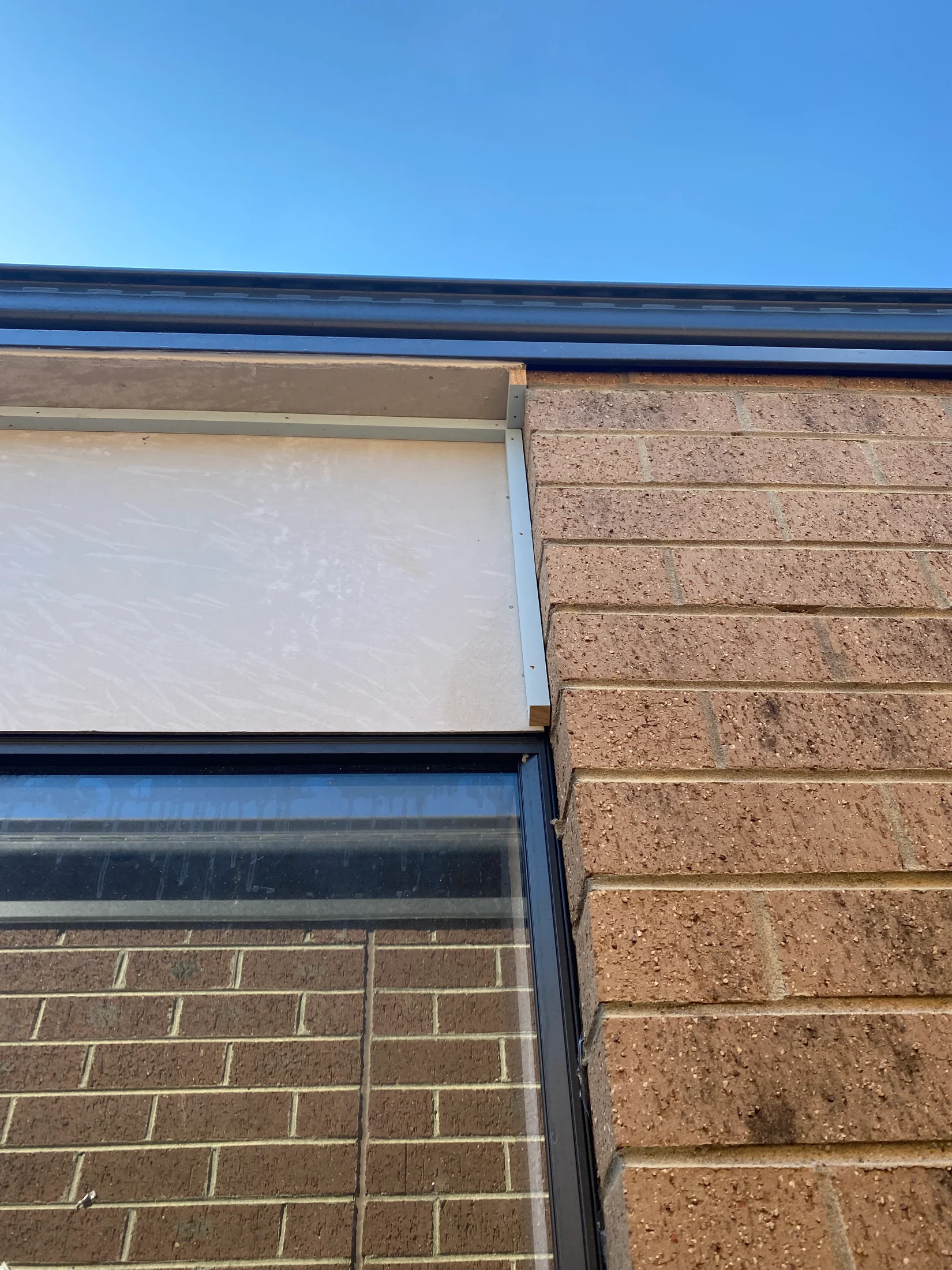 Brick wall with window reflecting the same wall. Clear blue sky above. No visible text. Calm and clear atmosphere.