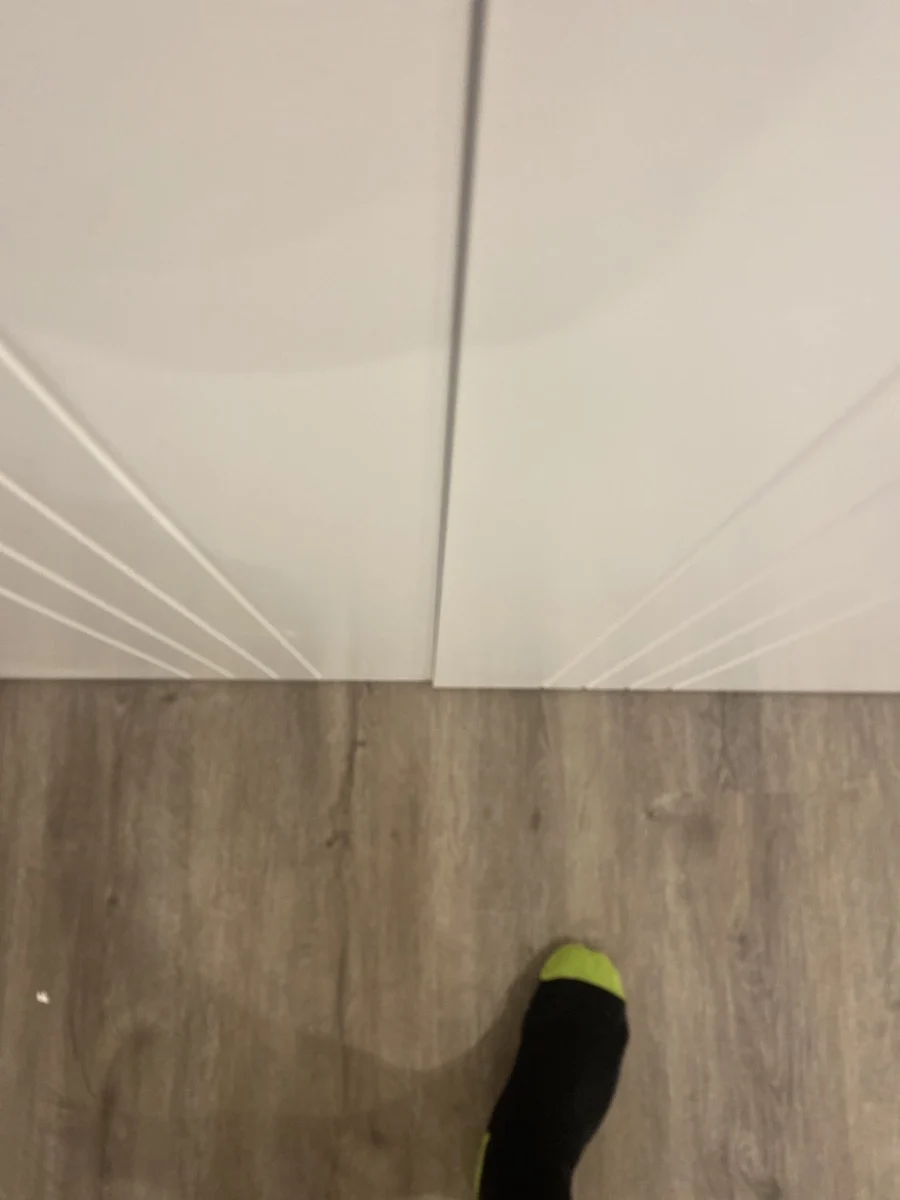 A foot in a black and green sock stands on a wooden floor in front of white cabinet doors, creating a simple, neutral setting.