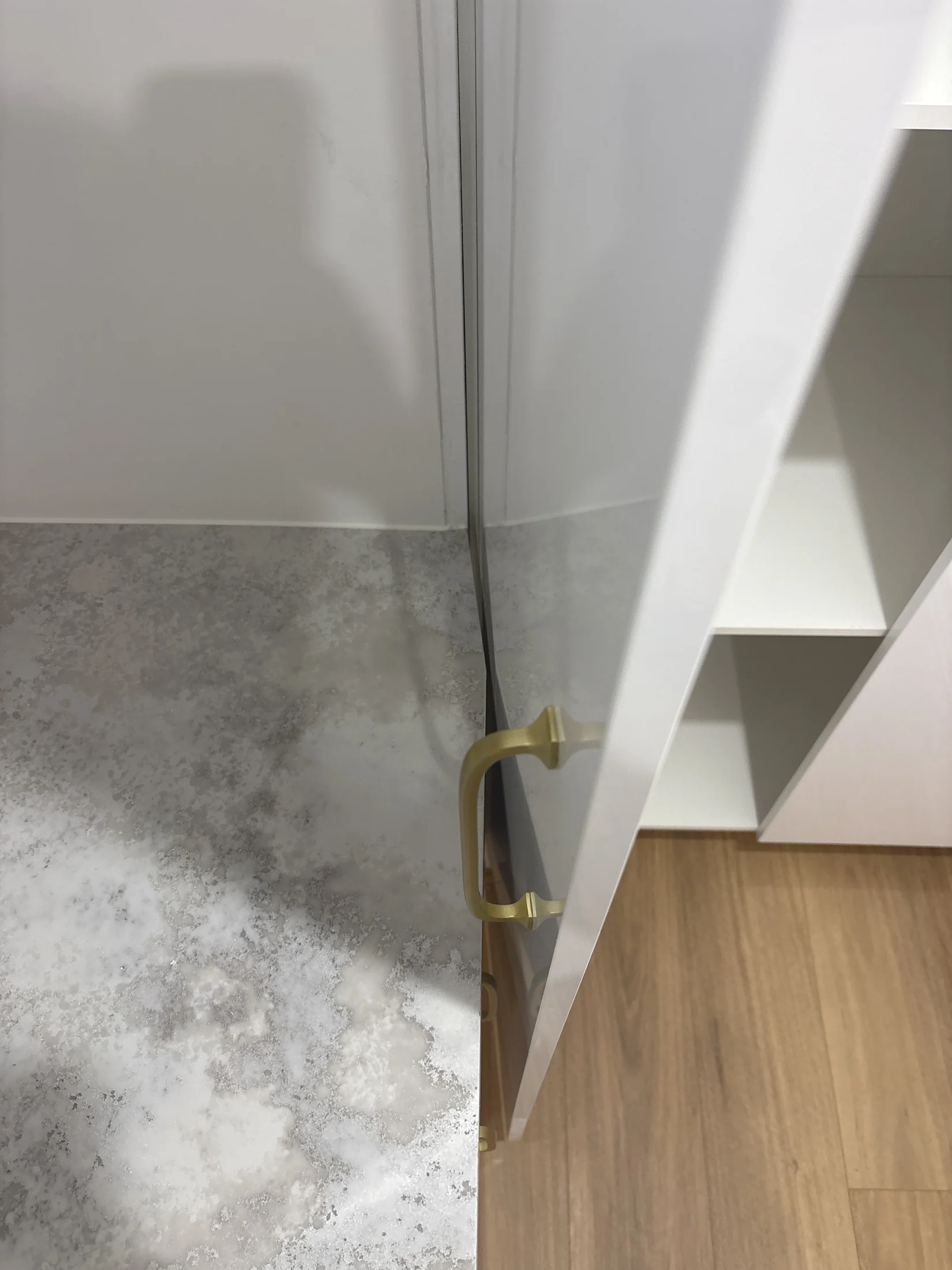 Marble-textured countertop meeting a white cabinet door with gold handle. Brown wooden floor visible. No text or people present.