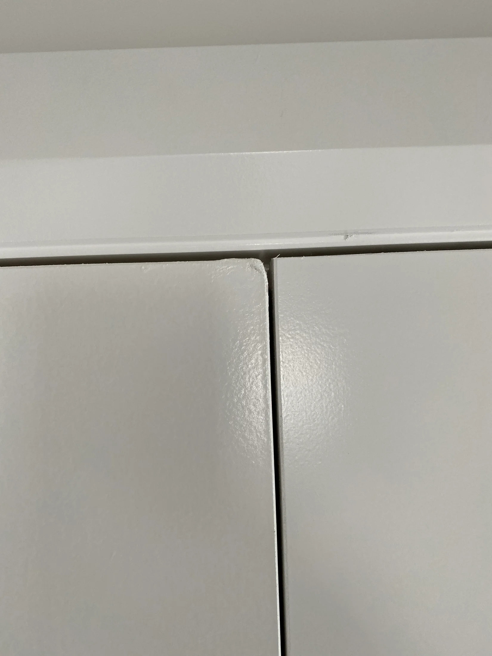 Close-up of two white cabinet doors with a narrow gap between them, set against a plain white wall. Smooth, glossy surface.