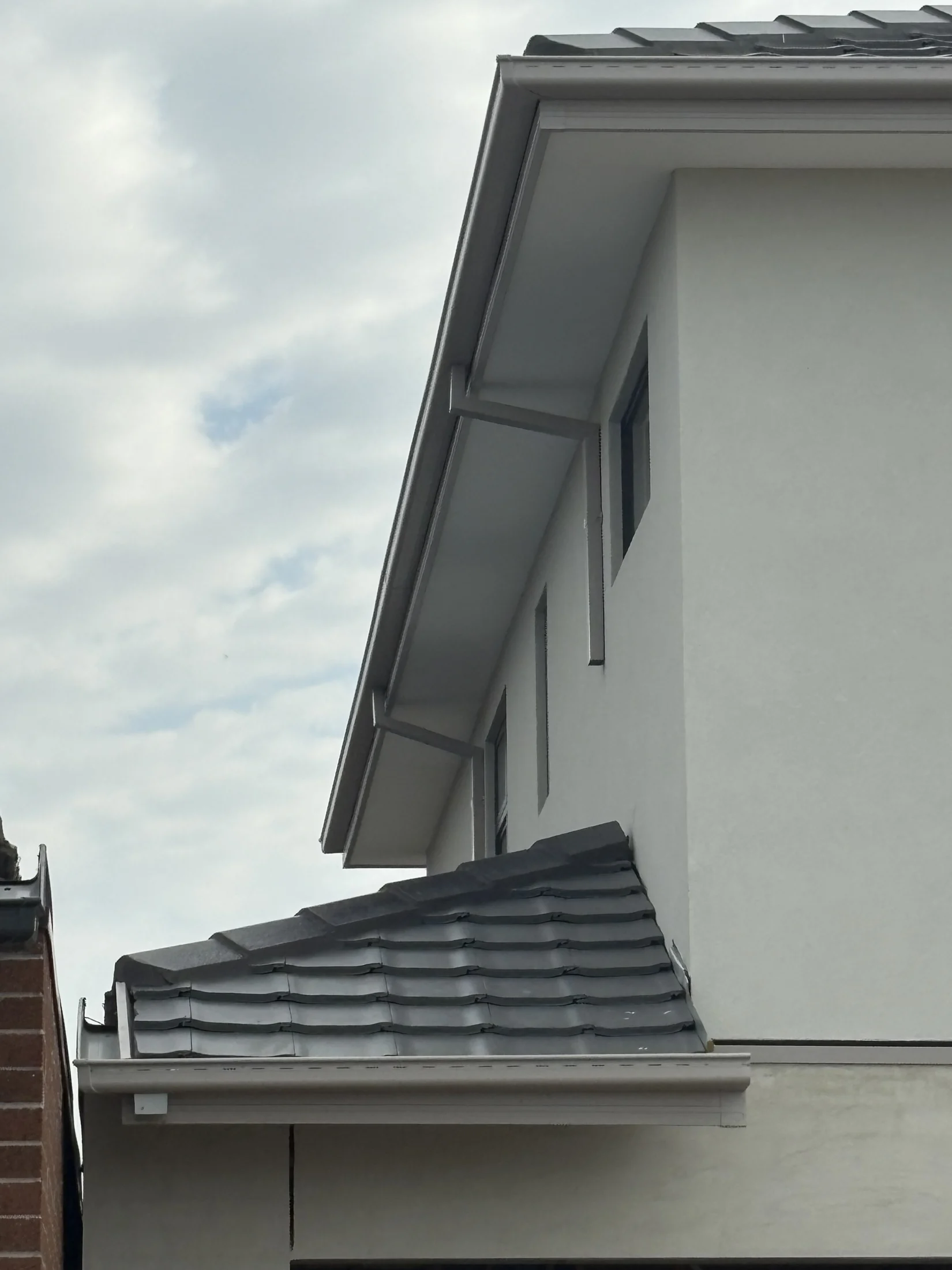 Modern house with gray tiled roof and white walls against a cloudy sky. Minimalist, clean design with a calm urban feel.