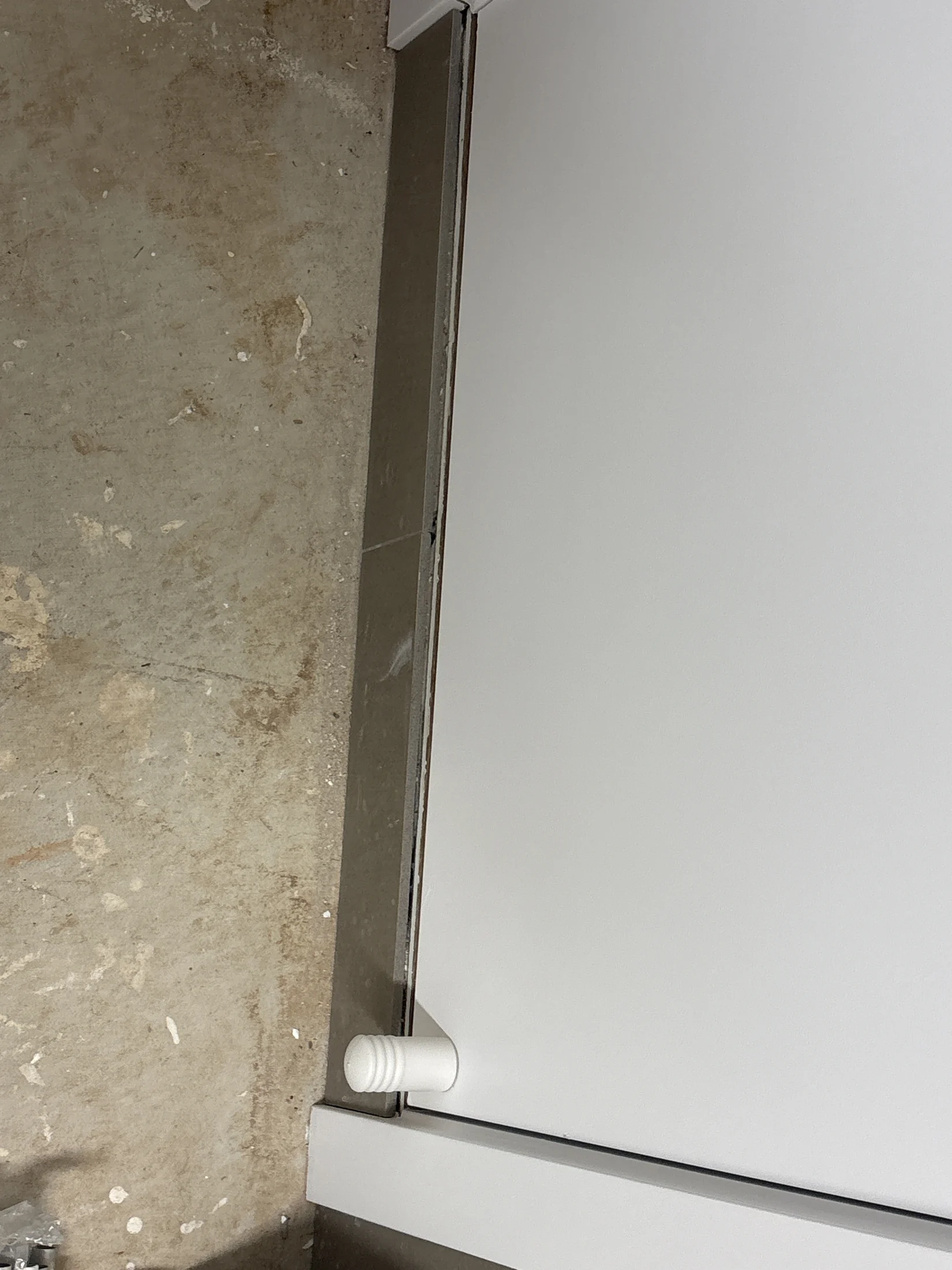 White door with a round handle, partially opened, against a textured, worn concrete floor. The setting appears industrial or unfinished.