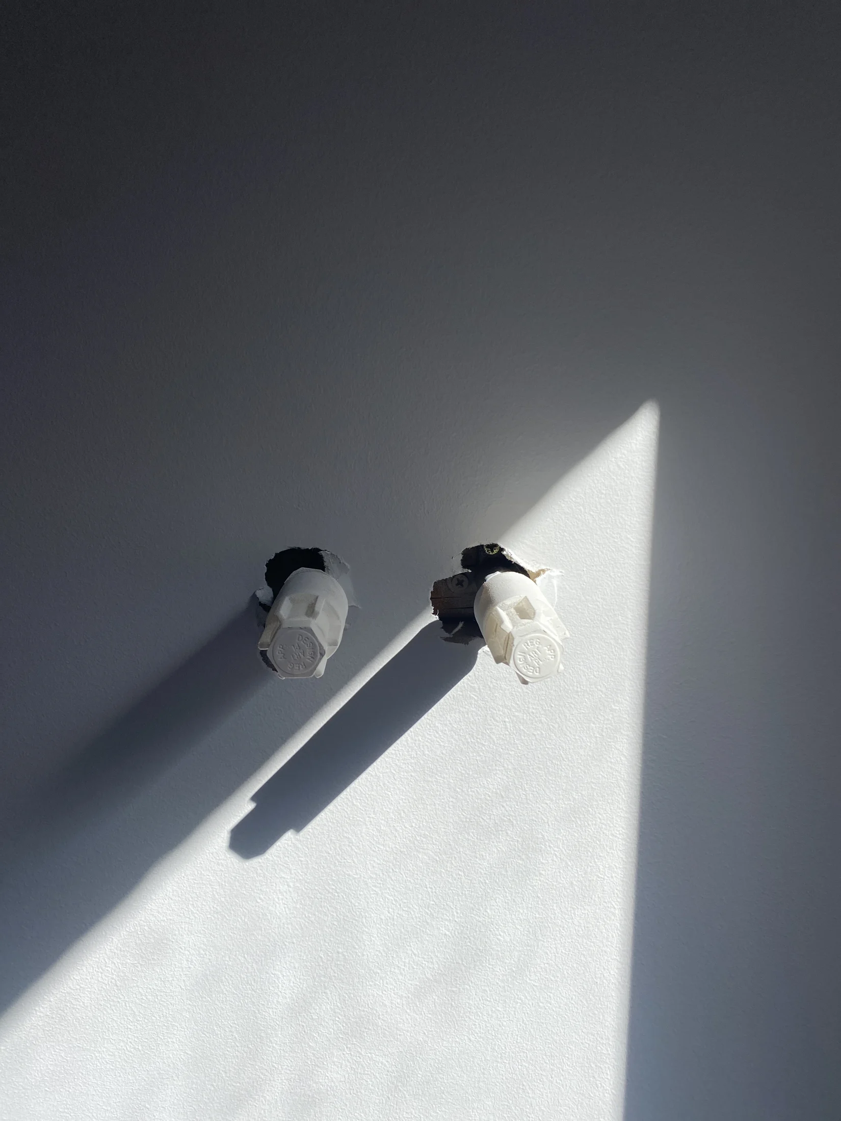 Two white protrusions on a wall cast long shadows in bright sunlight. The scene is minimalist with a calm, reflective mood.
