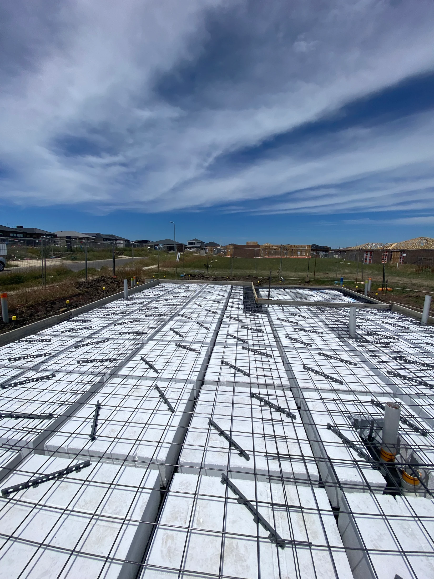 A concrete slab of a new home build set up, proper to pouring of the concrete with formwork, waffle pods, reinforcement and temporary fencing viewable.