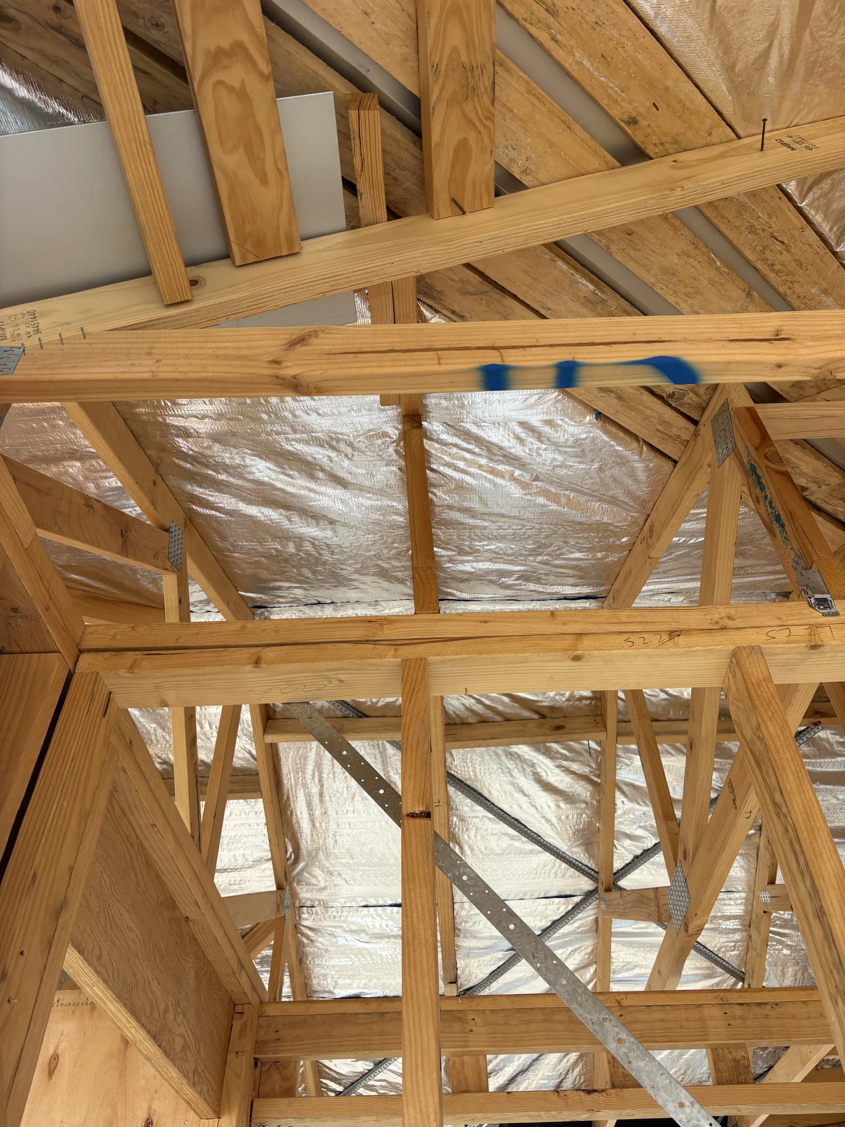 Wooden roof framing under construction with metal braces. Silver insulation is visible between beams. Bright and orderly setting.