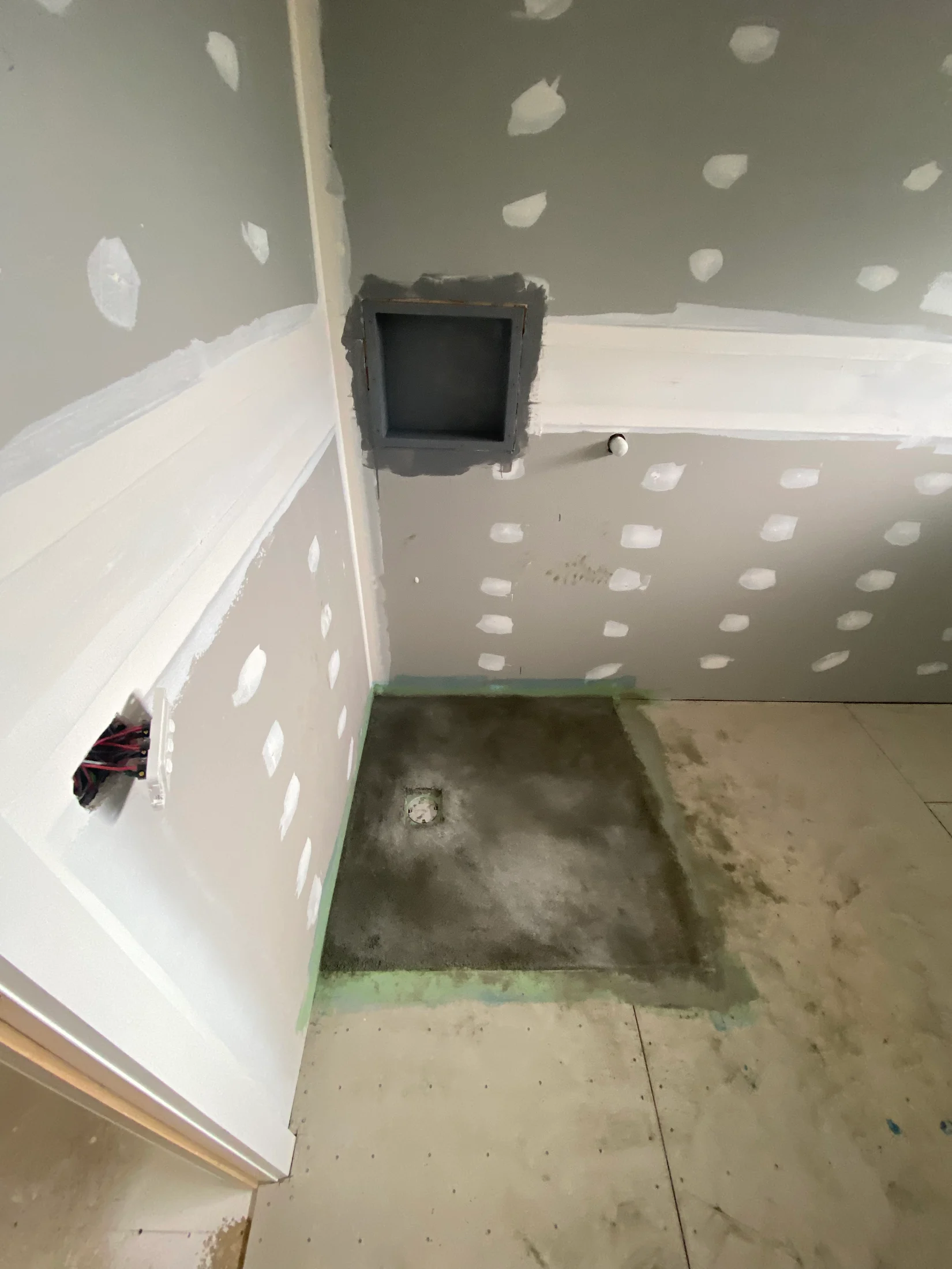Unfinished room with drywall and patches, a square cut-out on the floor, wires exposed, and a partially painted wall; appears under construction.