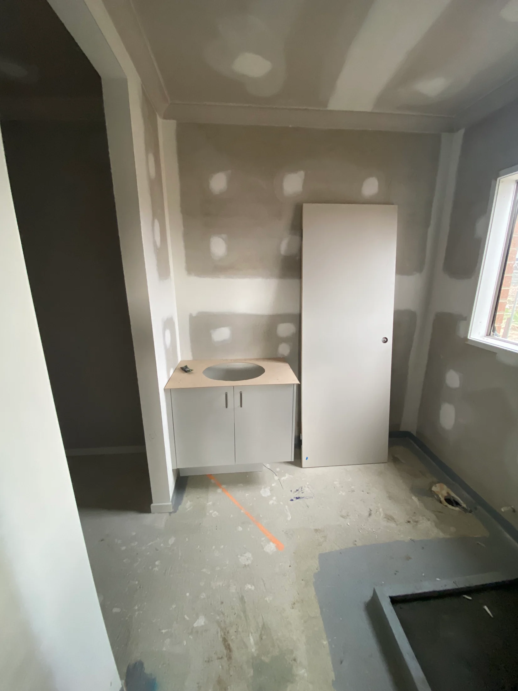 Unfinished bathroom with unpainted drywall, a small vanity without a sink, a standing cabinet, and a window letting in natural light.