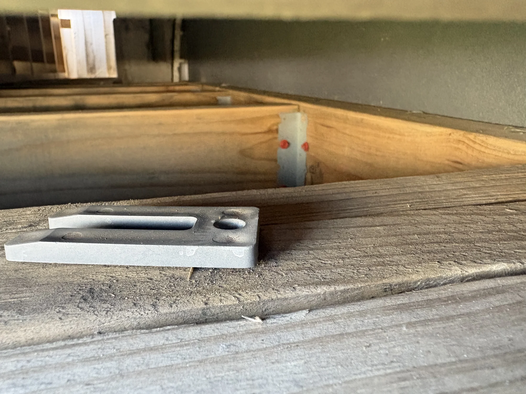 Metal bracket on wooden beams, surrounded by wood and tools, in a workshop setting. Natural wood grain and grey hues dominate the scene.