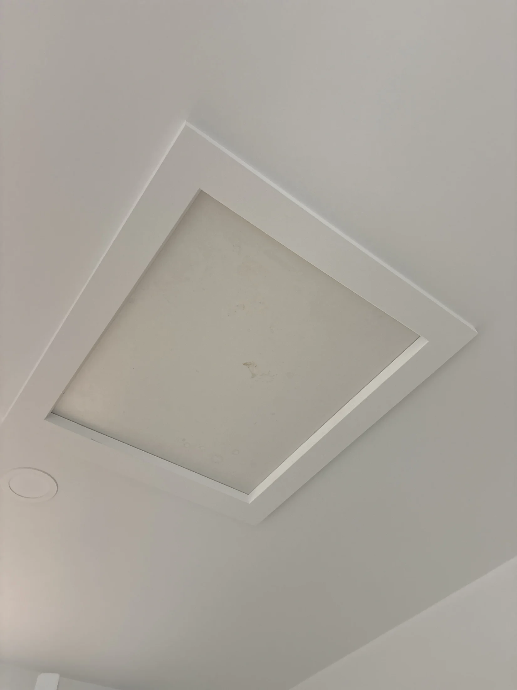 White ceiling with a rectangular panel and faint stains. Minimalist design with soft lighting, creating a clean and neutral atmosphere.