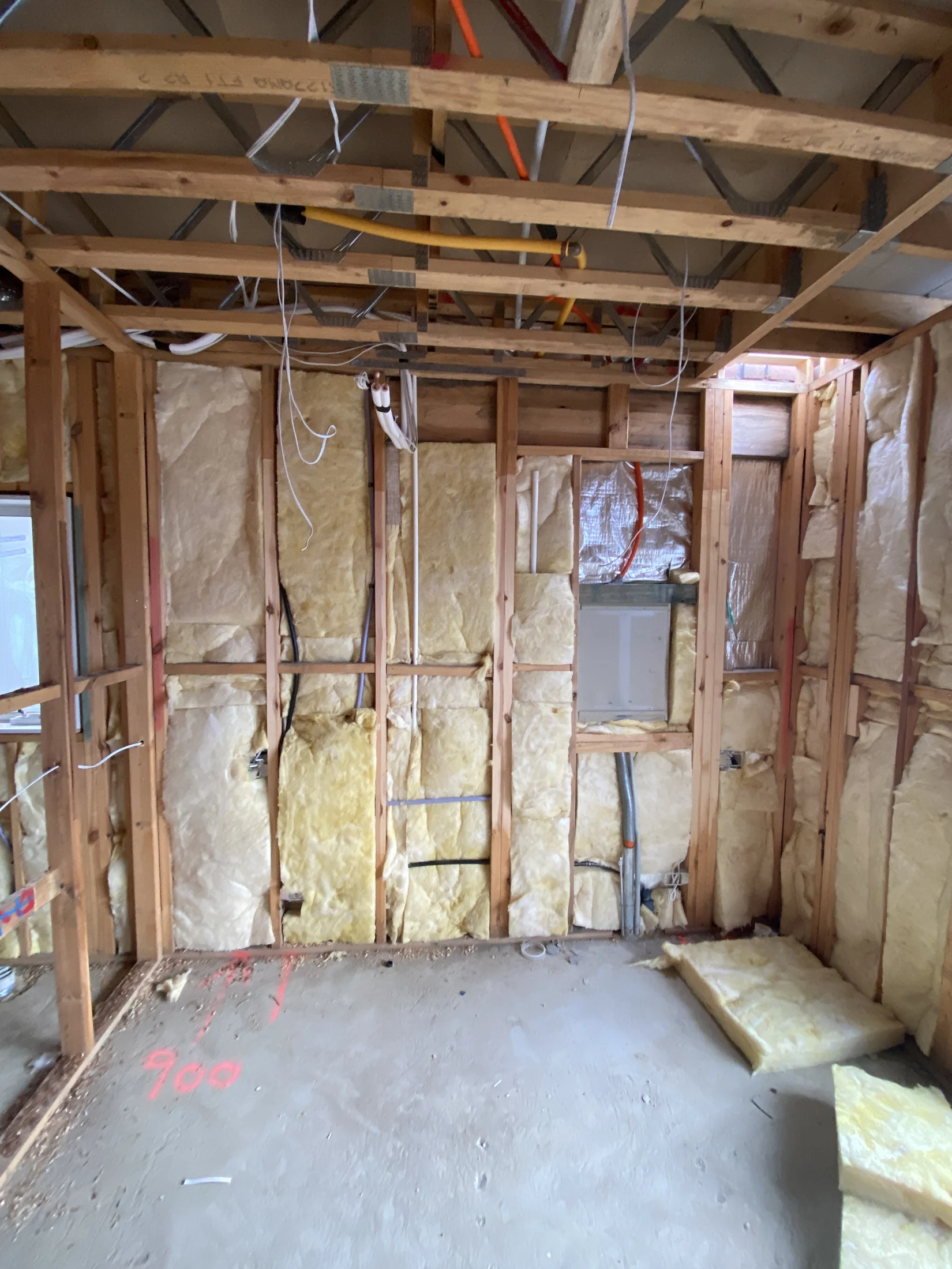 Unfinished room with exposed wooden frame, insulation, and wiring. Yellow and red cables visible. Floor marked with red text "900".