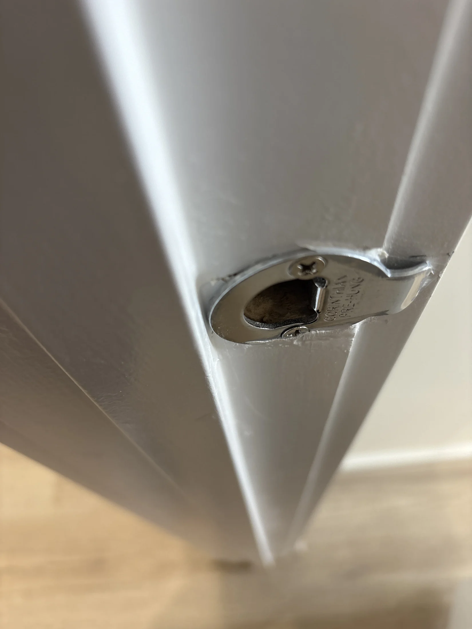 Close-up of a white door with a silver latch and visible text, against a wooden floor background.